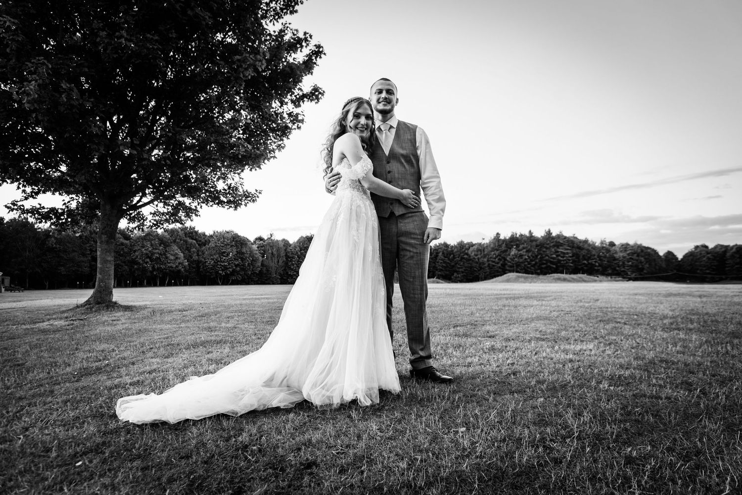A series of black and white wedding photos showing a couple in formal attire posing together in an outdoor field setting.