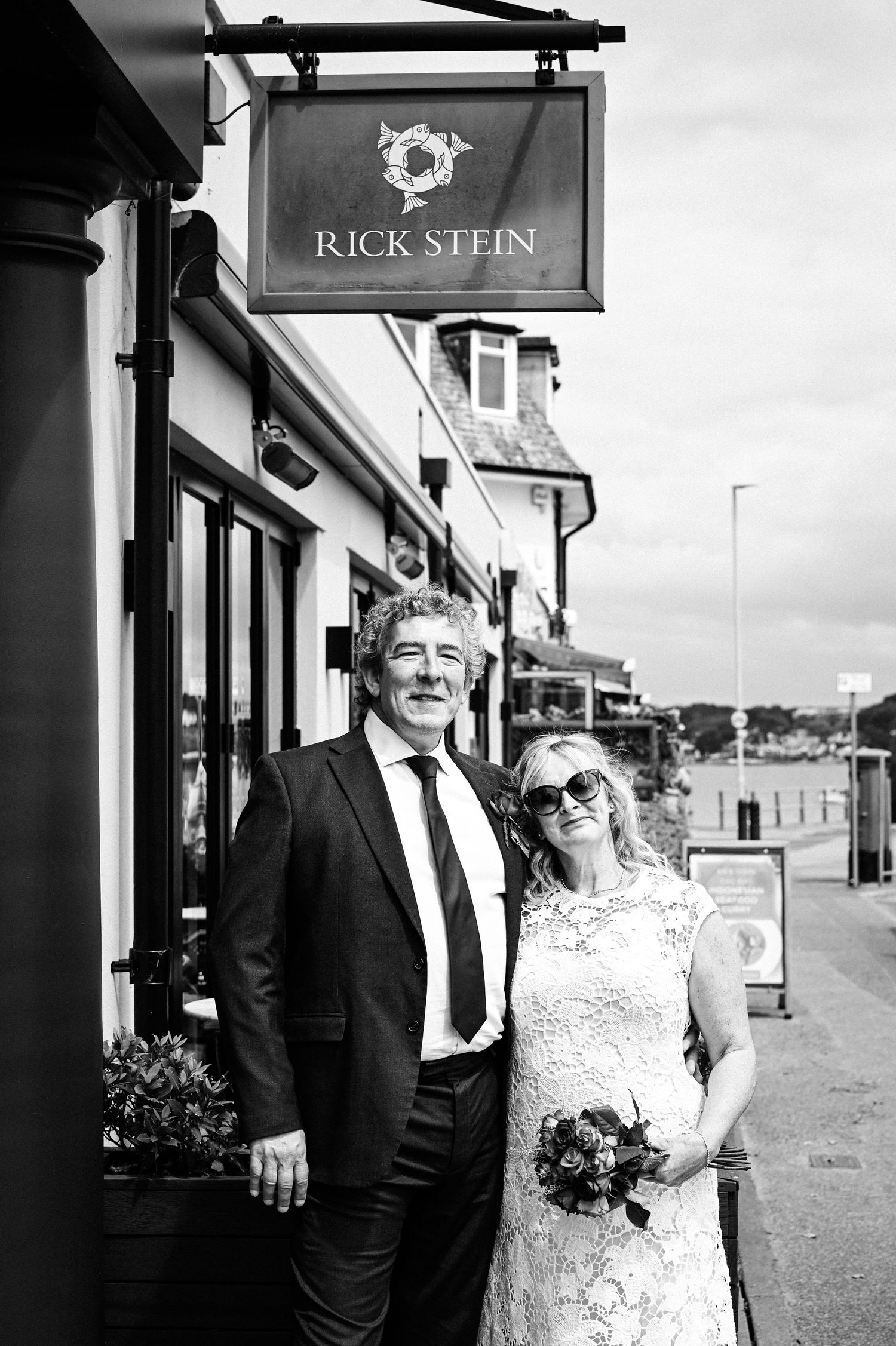 Bride and groom posing outside Rick Stein restaurant in black and white wedding photo.