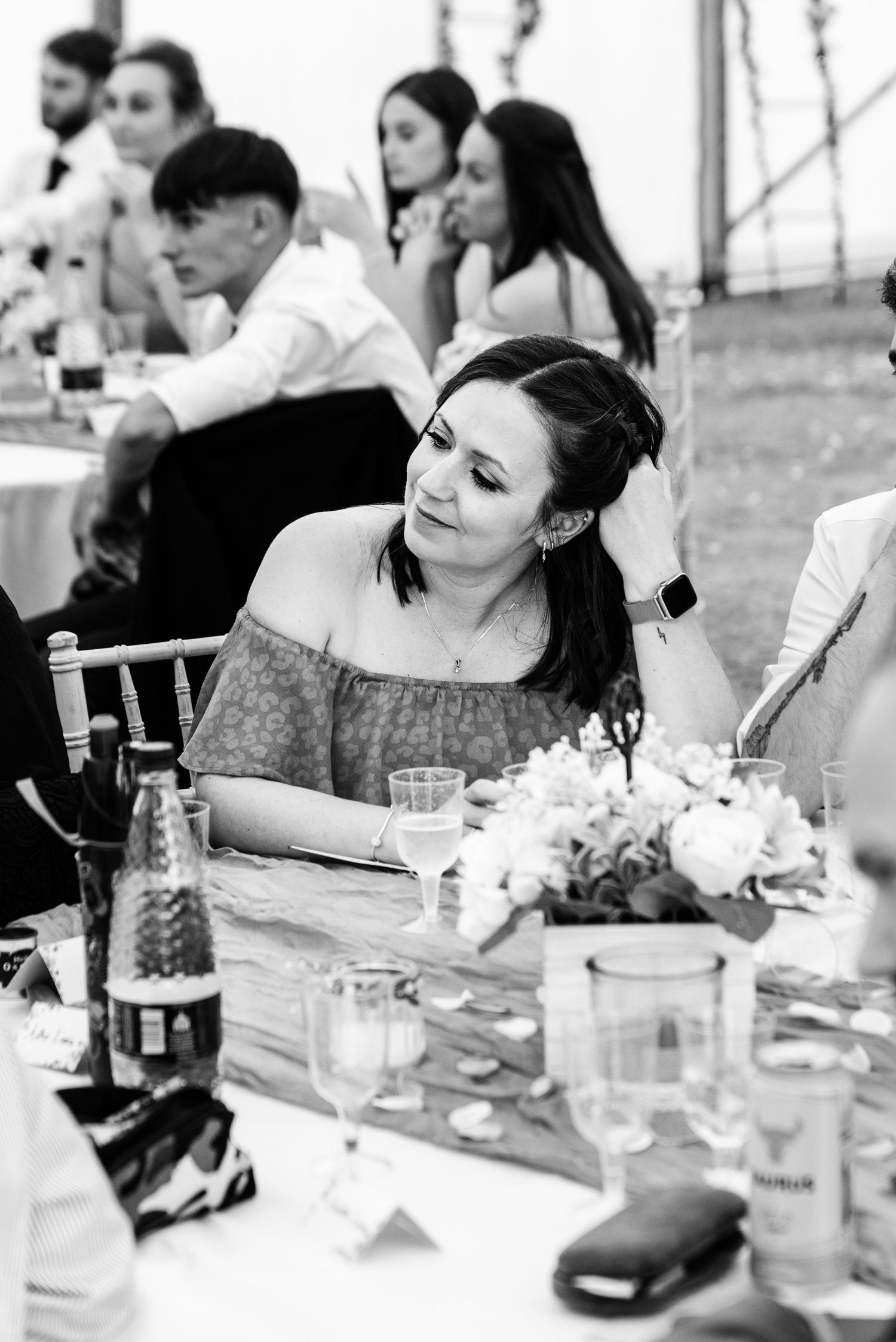 Black and white candid of smiling female wedding guest seated at decorated reception table.