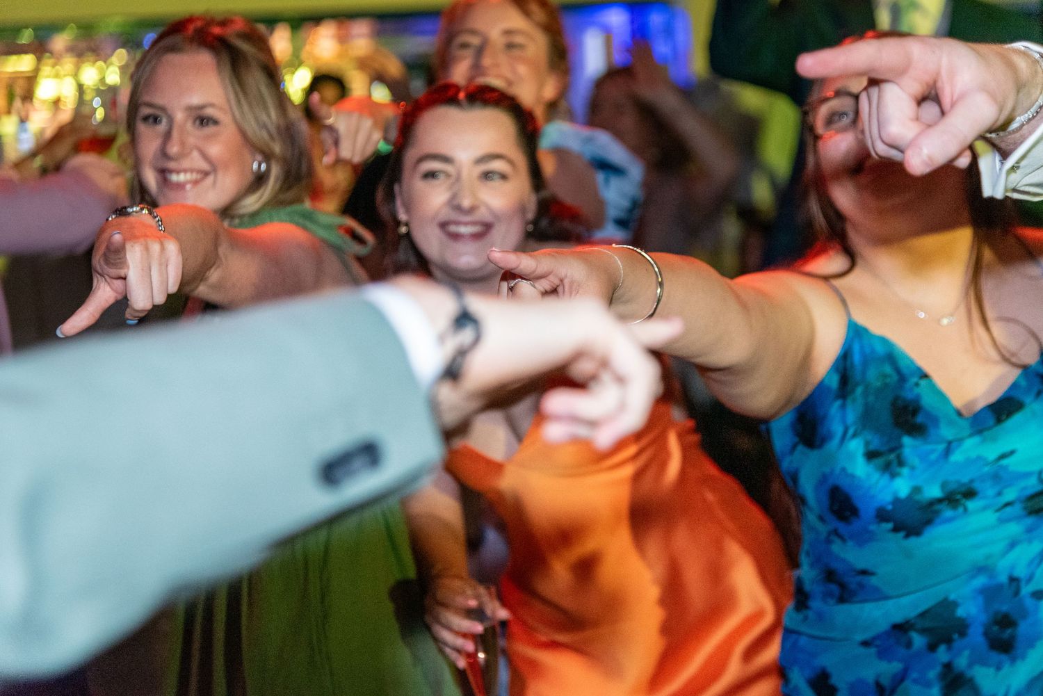 Group of women in colorful dresses smiling and pointing at a lively party or event celebration.