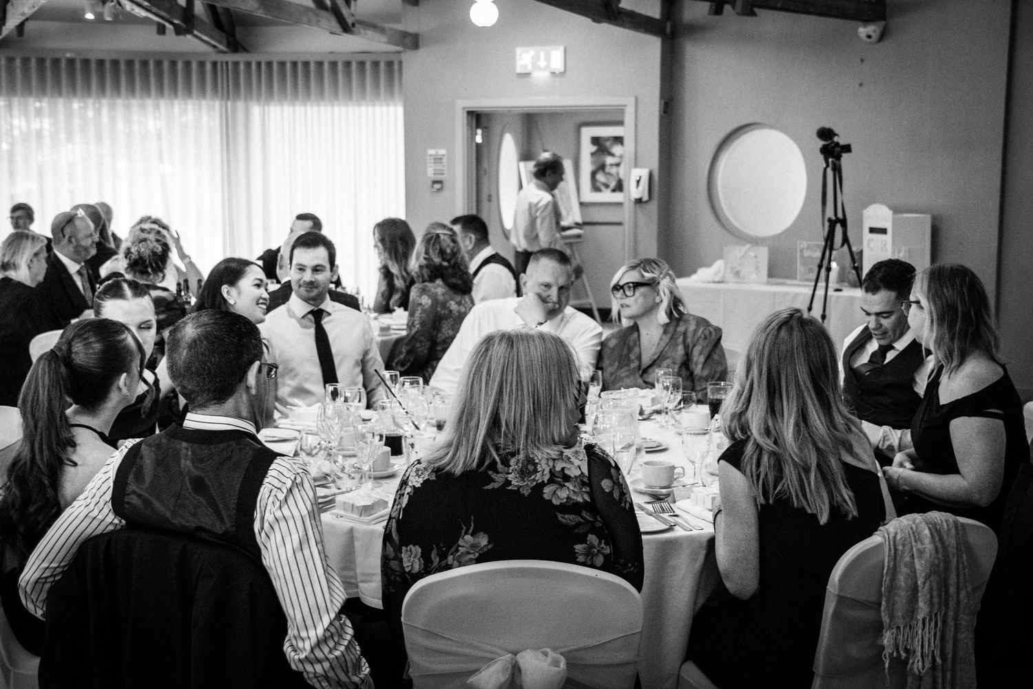 Black and white photo of wedding guests seated at round tables during a reception dinner.