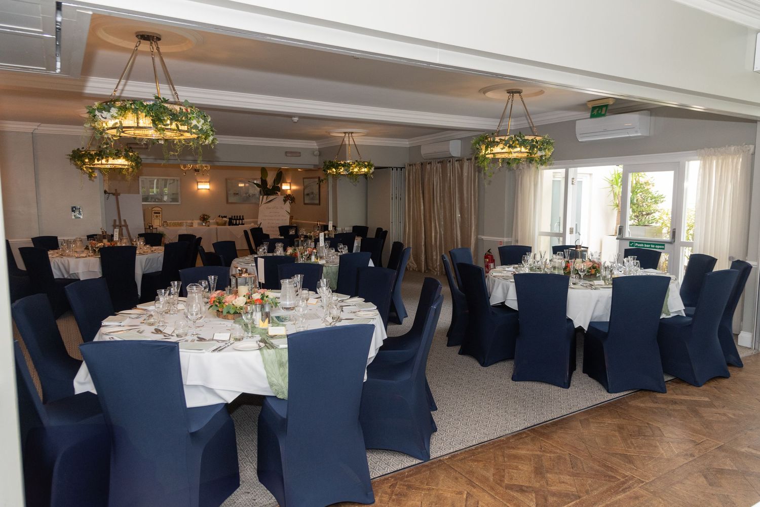 Elegant banquet hall with round tables, navy blue chair covers, white linens, and stained glass chandeliers for events.