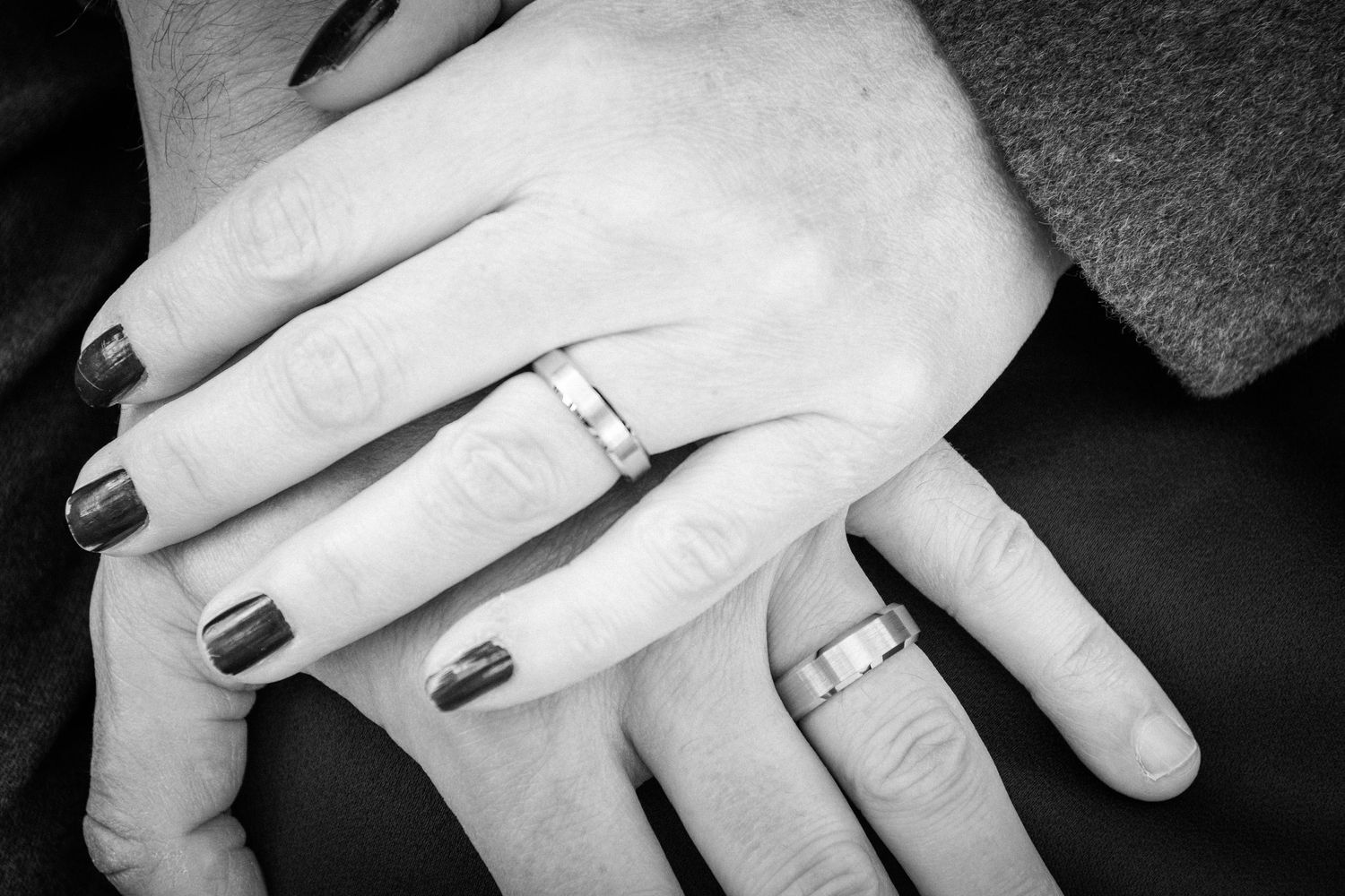 Black and white photo showing multiple hands wearing wedding rings in a sequence.
