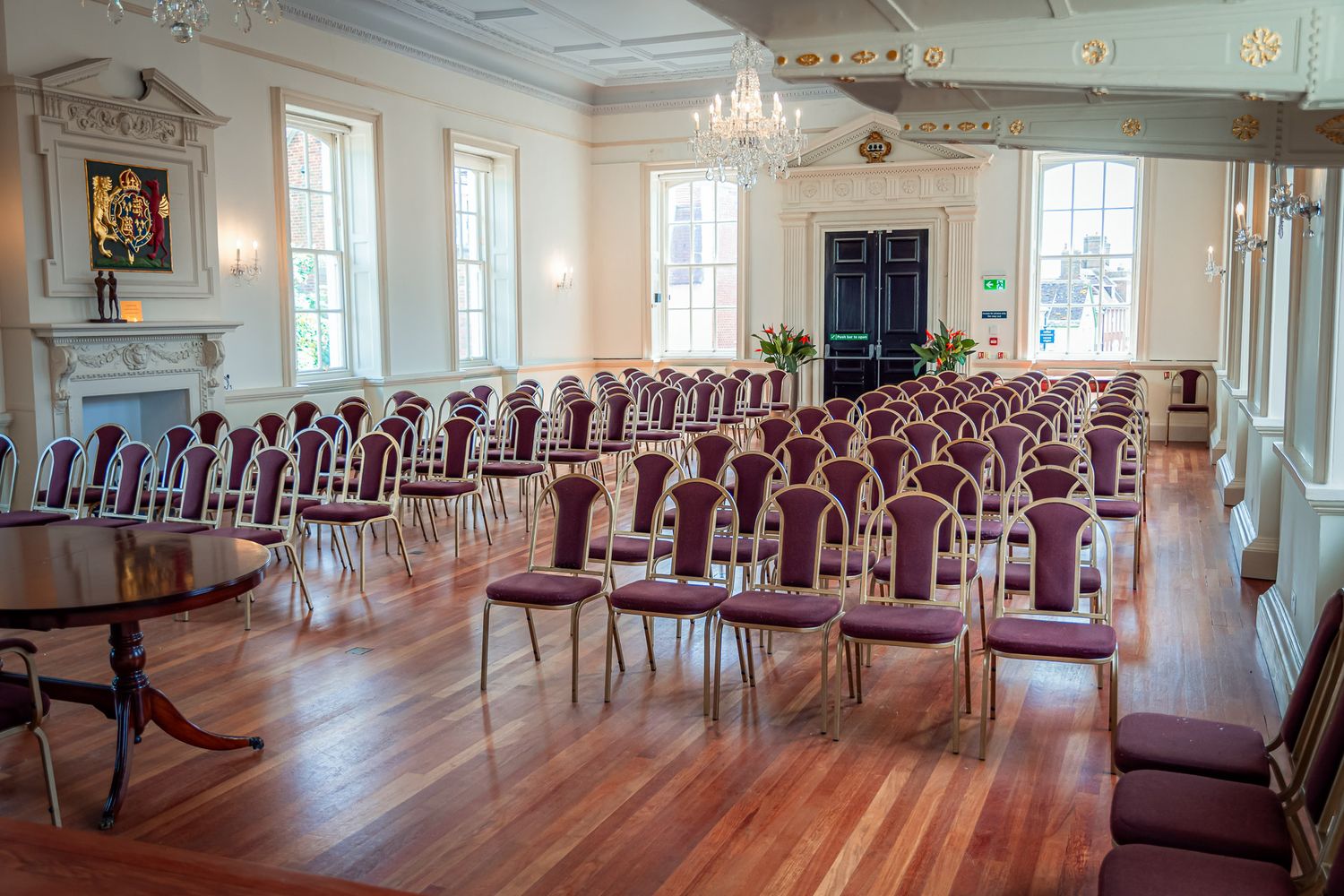 Elegant banquet hall with rows of mahogany chairs, ornate chandelier, and hardwood floors in a historic building.