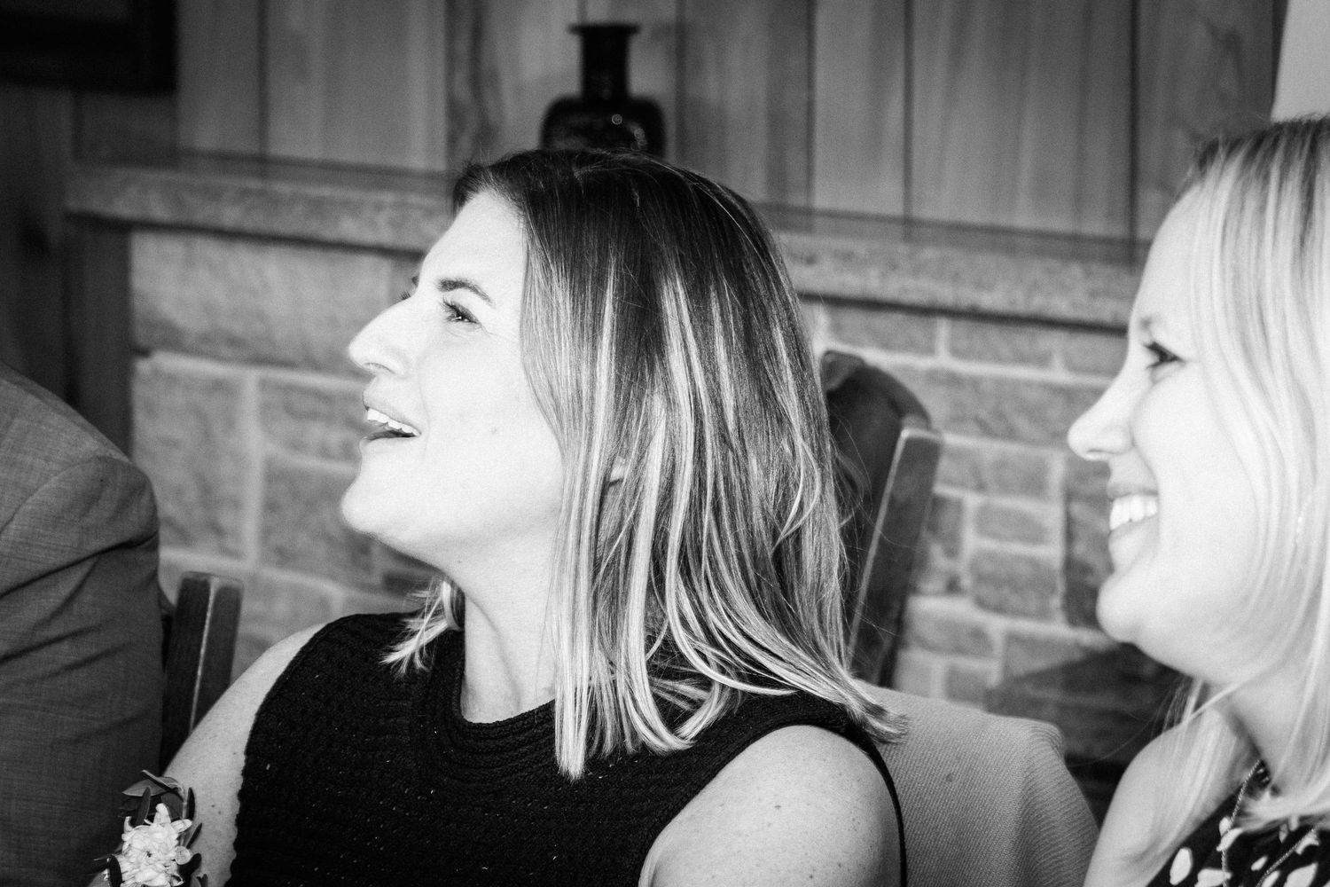 Two women laughing and smiling together in a candid black and white photo at a social gathering.