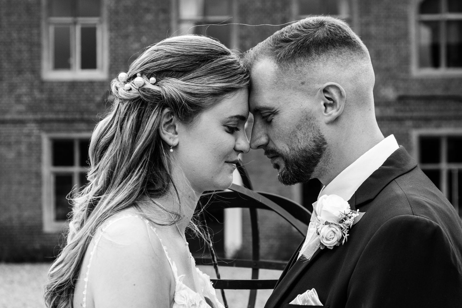 Black and white wedding photos show romantic moments between a bride and groom in front of a brick building.