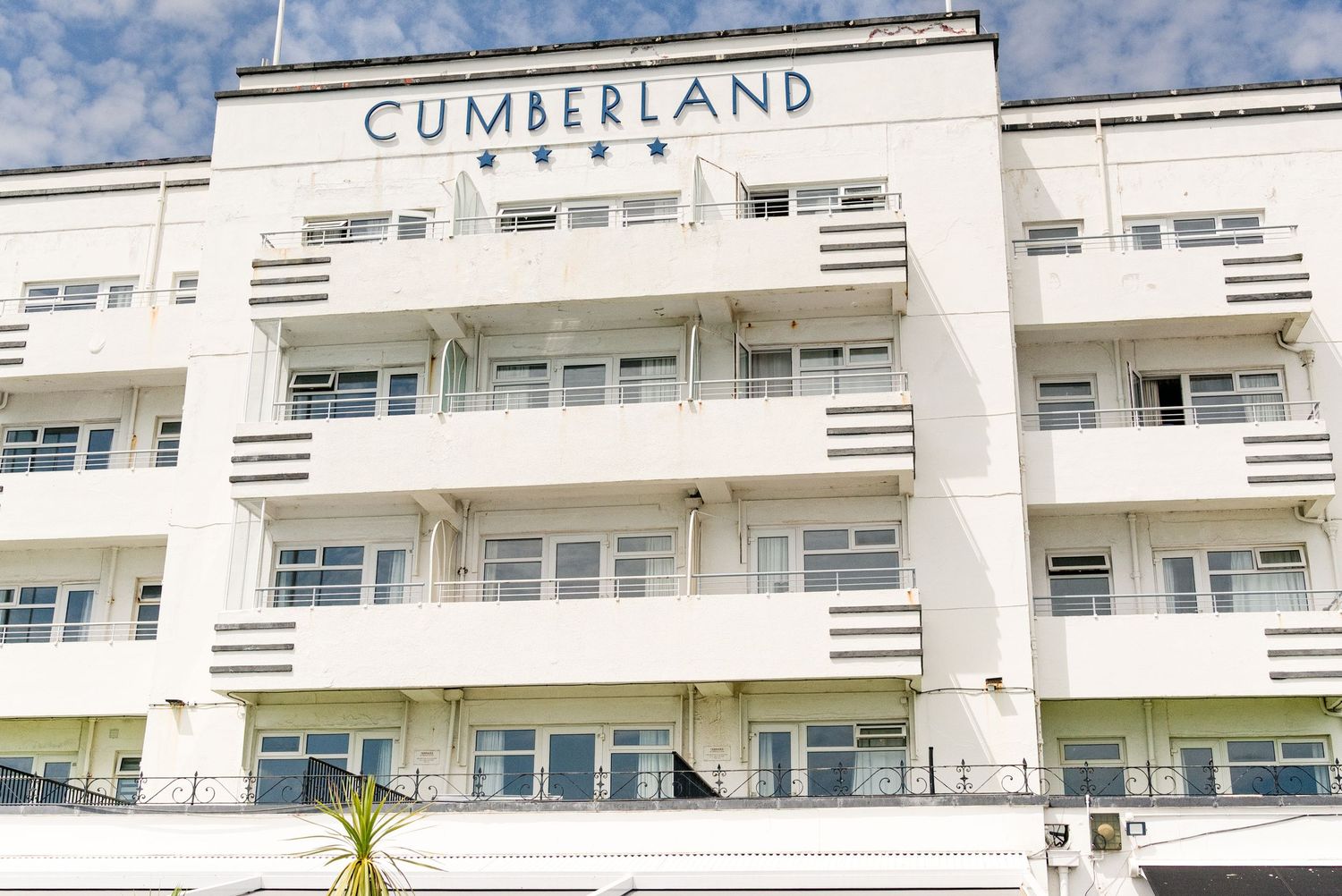 Exterior view of the Cumberland Hotel, a white Art Deco building with balconies and four-star rating displayed on facade.