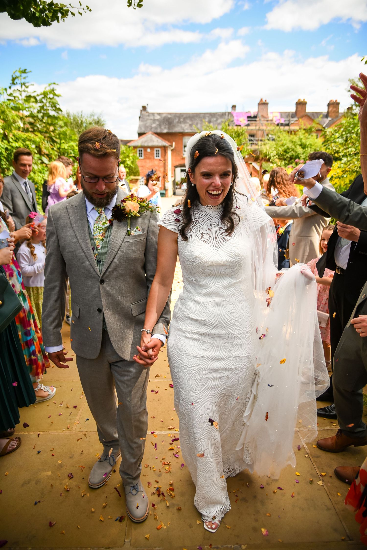 A joyful bride and groom walk hand-in-hand through a confetti shower at their outdoor wedding ceremony.