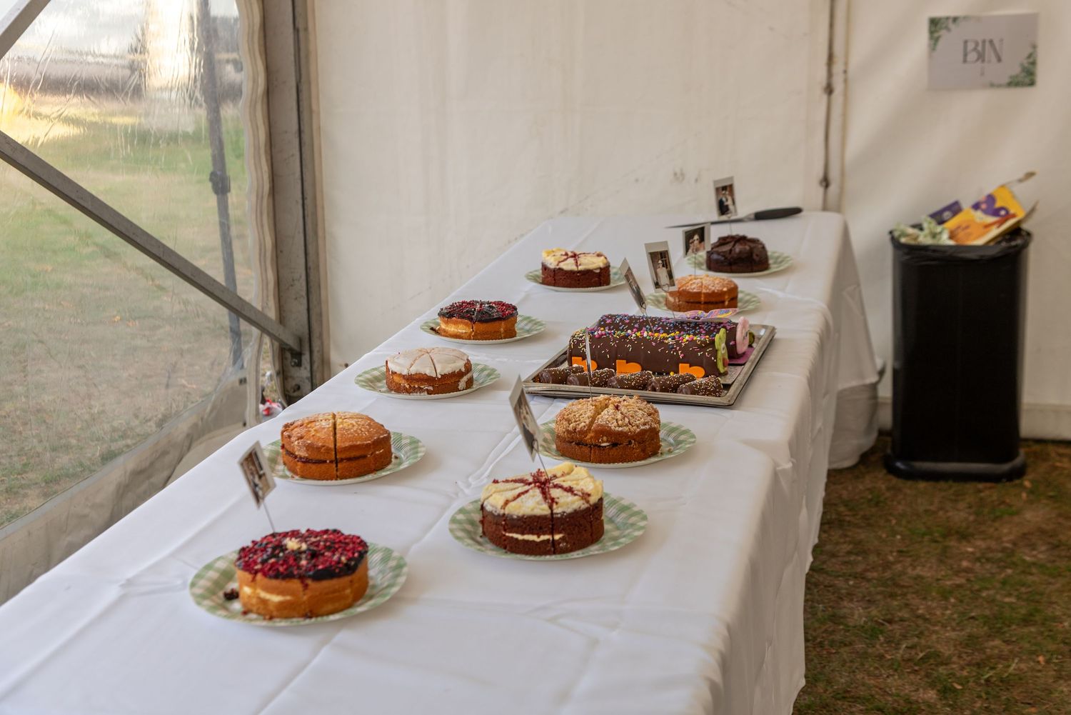 A display of homemade cakes on a white tablecloth inside a marquee tent at an outdoor baking competition.