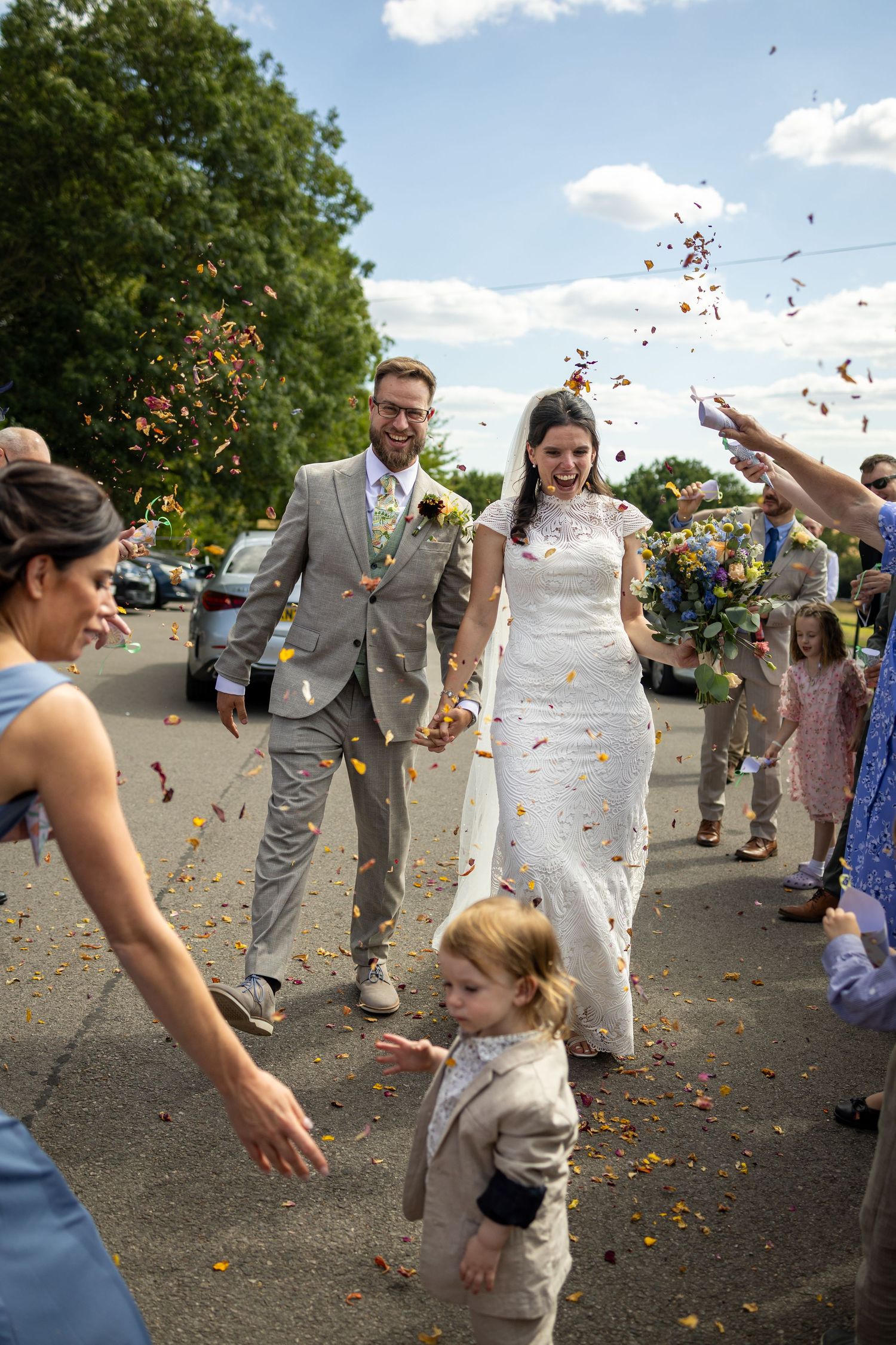 Bride and groom walking through colorful confetti shower with guests celebrating outdoors on their wedding day.