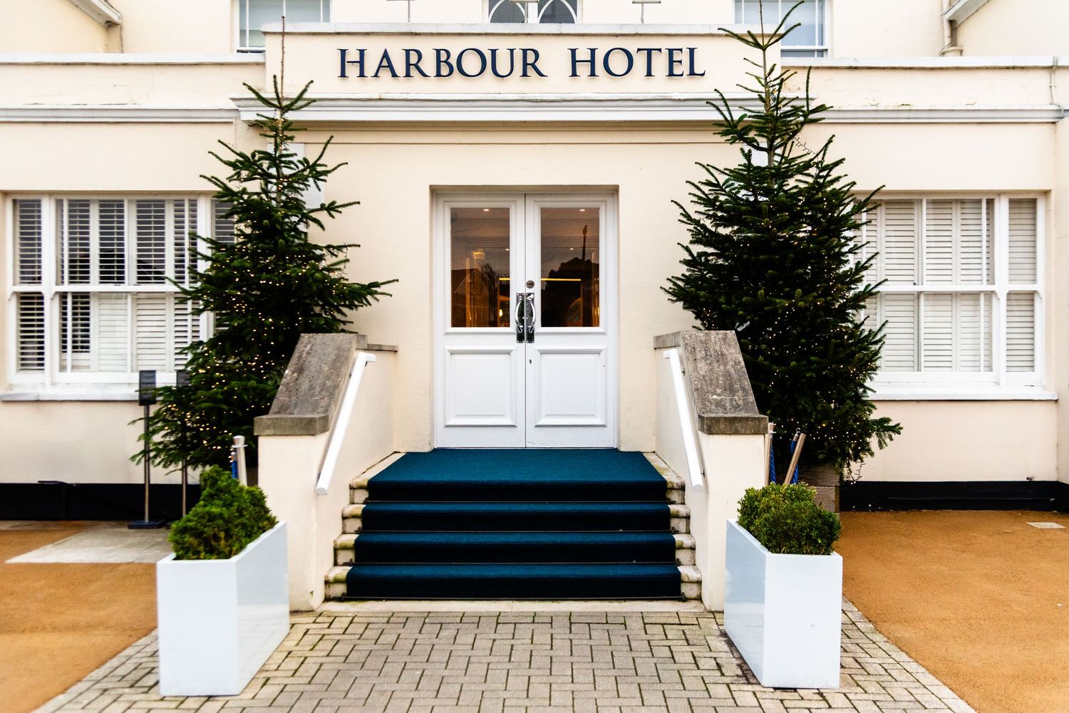 A row of exterior hotel building facades with evergreen trees and white columns along the entrance.