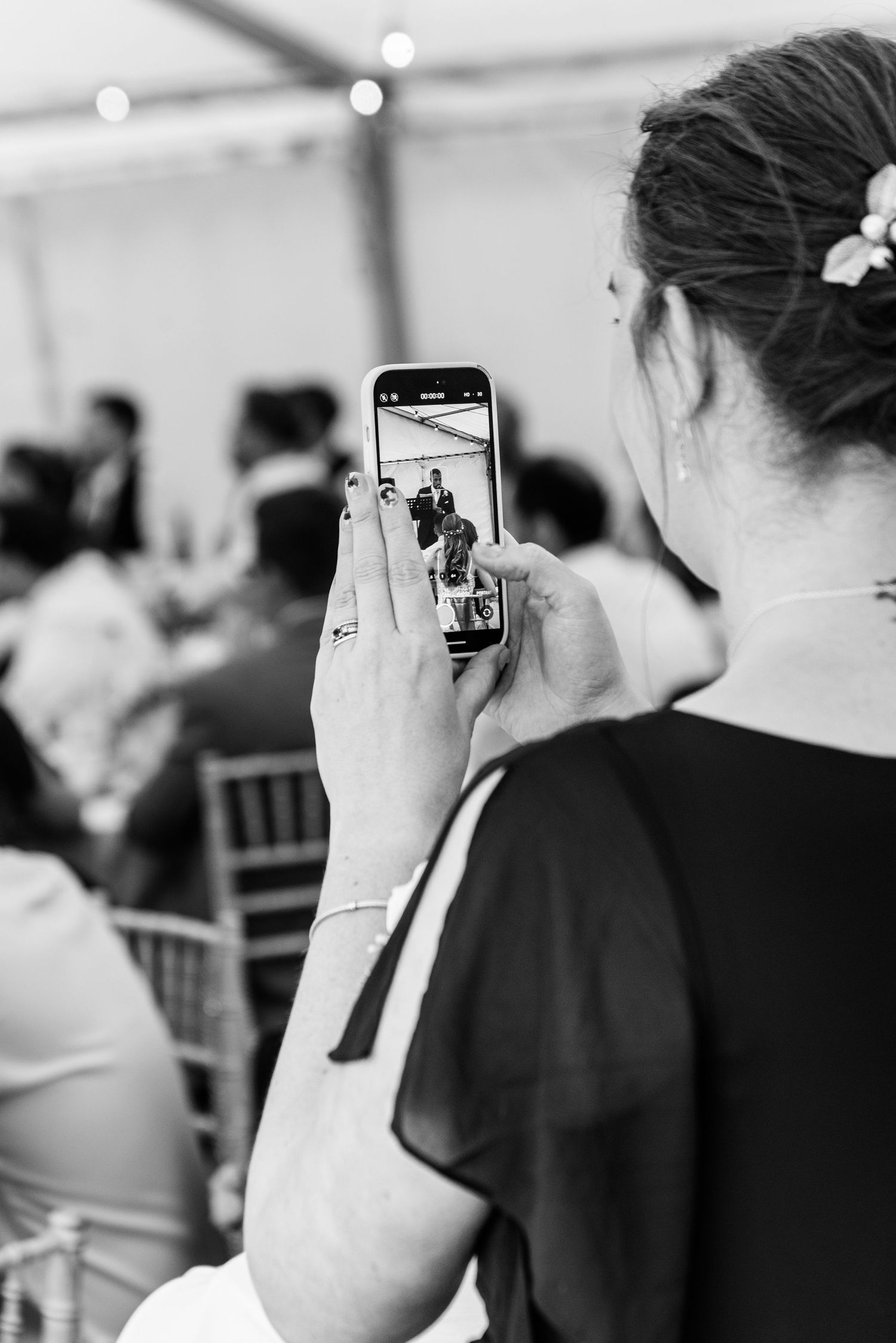 Wedding guest photographs ceremony procession on smartphone in black and white candid shot.