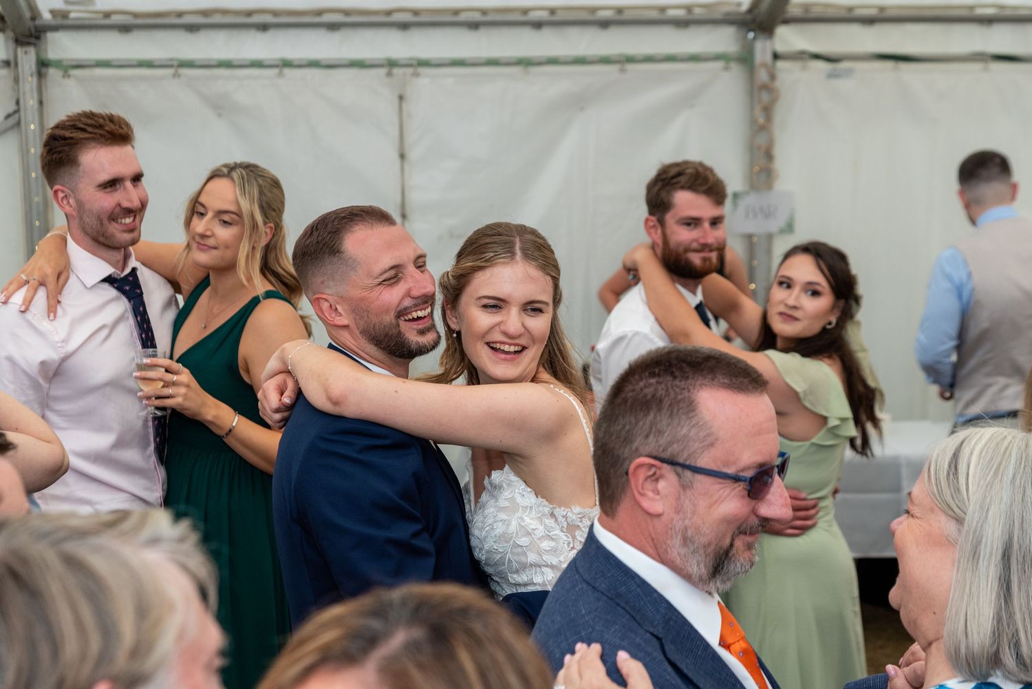 Bride in white gown hugging guests and laughing during lively wedding reception.