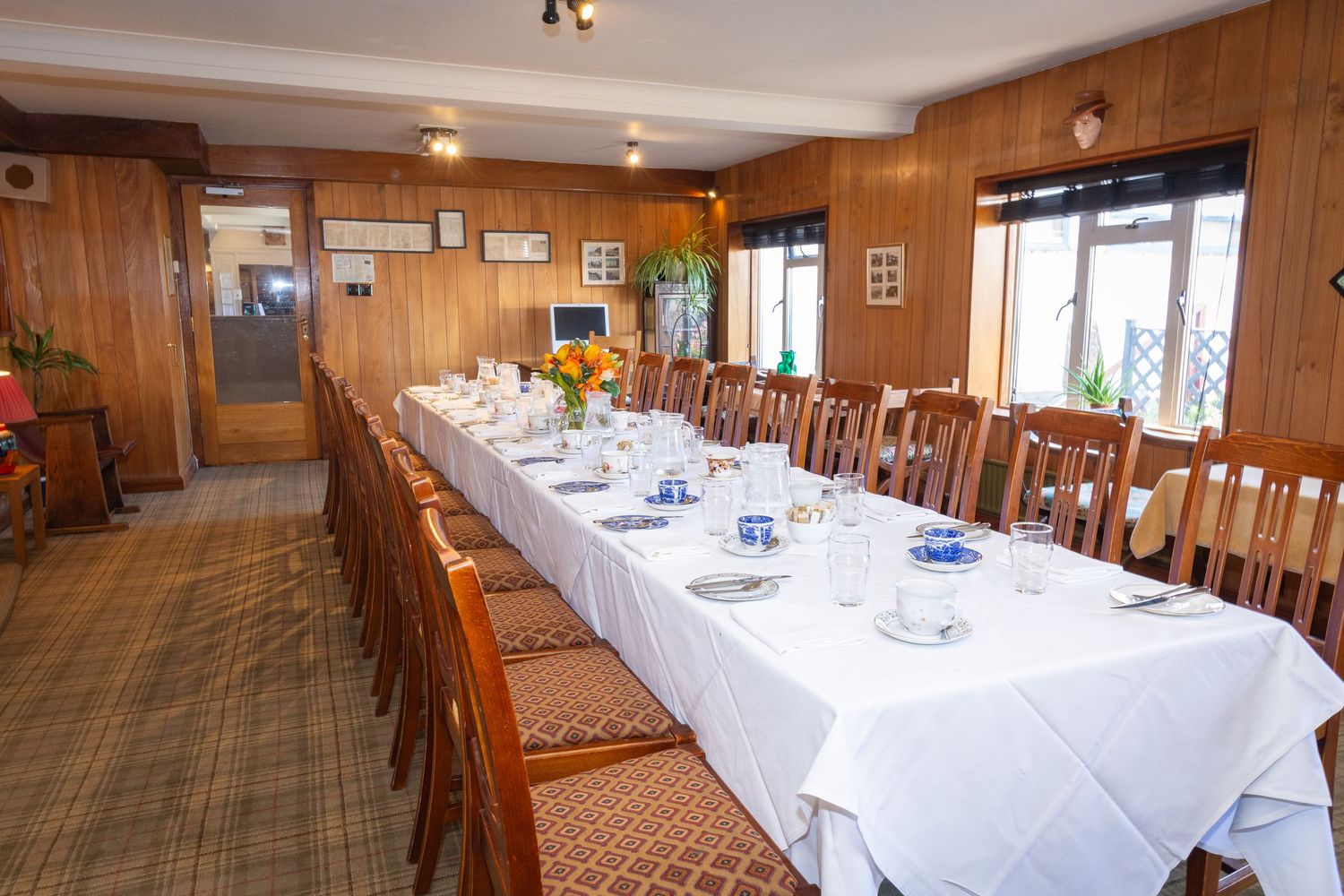 Long wooden banquet tables with white tablecloths set up in a rustic dining room with wood-paneled walls.