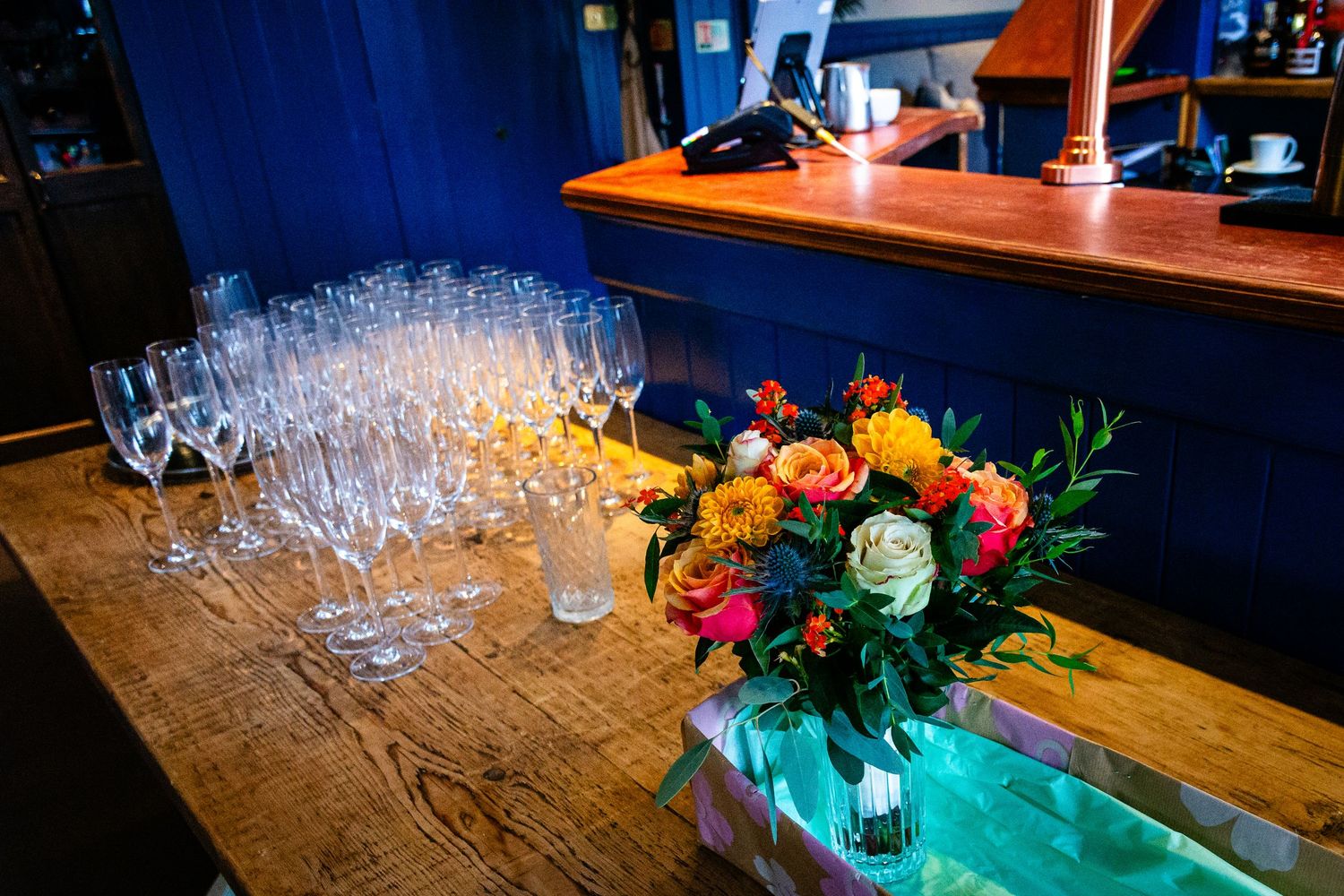 Elegant wedding reception bar setup with champagne flutes and colorful floral centerpiece.