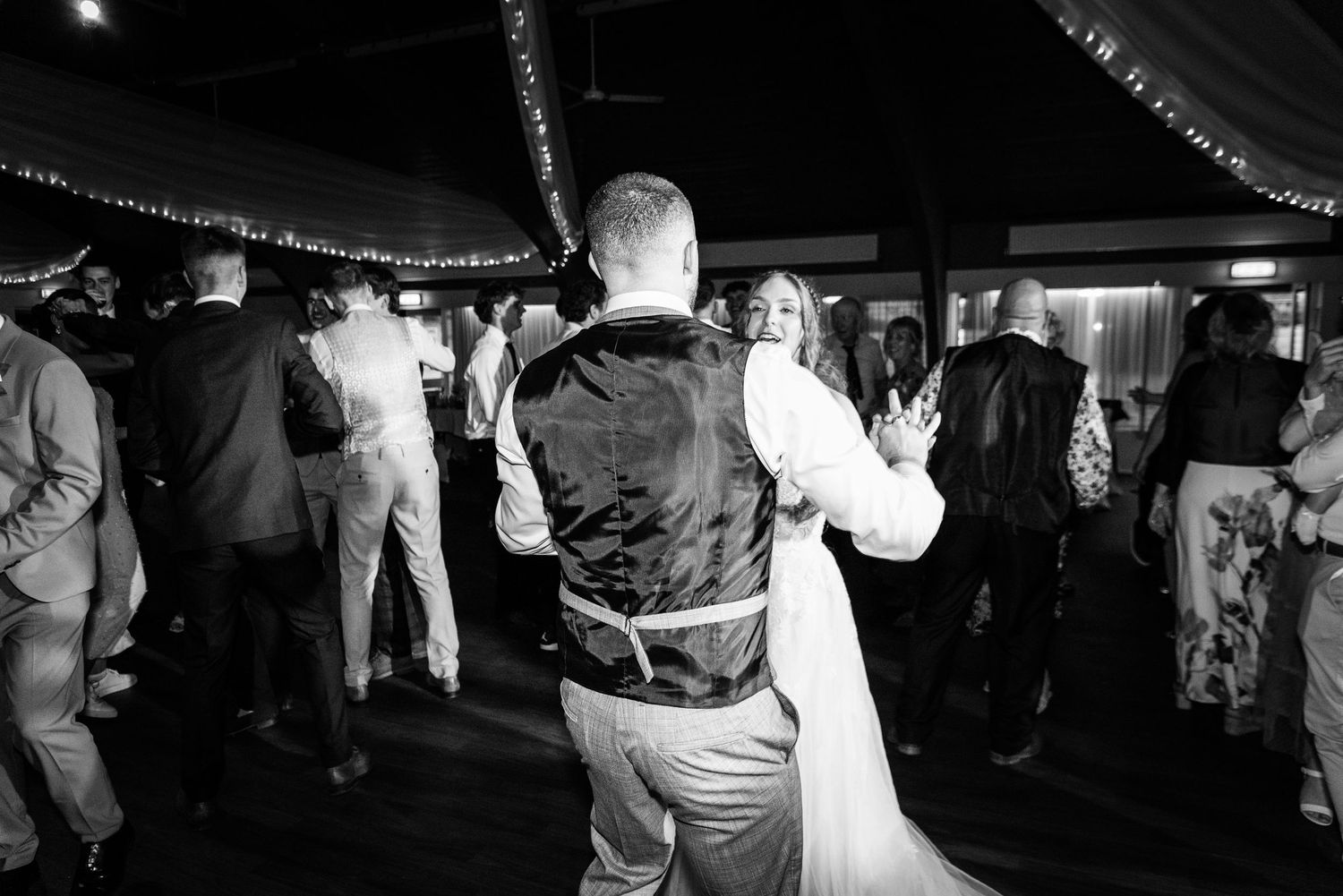 Bride and groom share first dance surrounded by guests on decorated wedding reception dance floor.