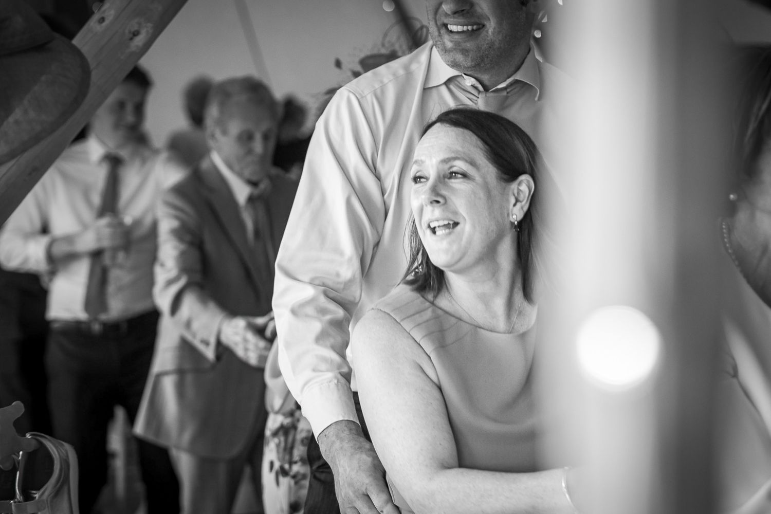 A woman laughs joyfully while dancing with a partner at a wedding reception in black and white.
