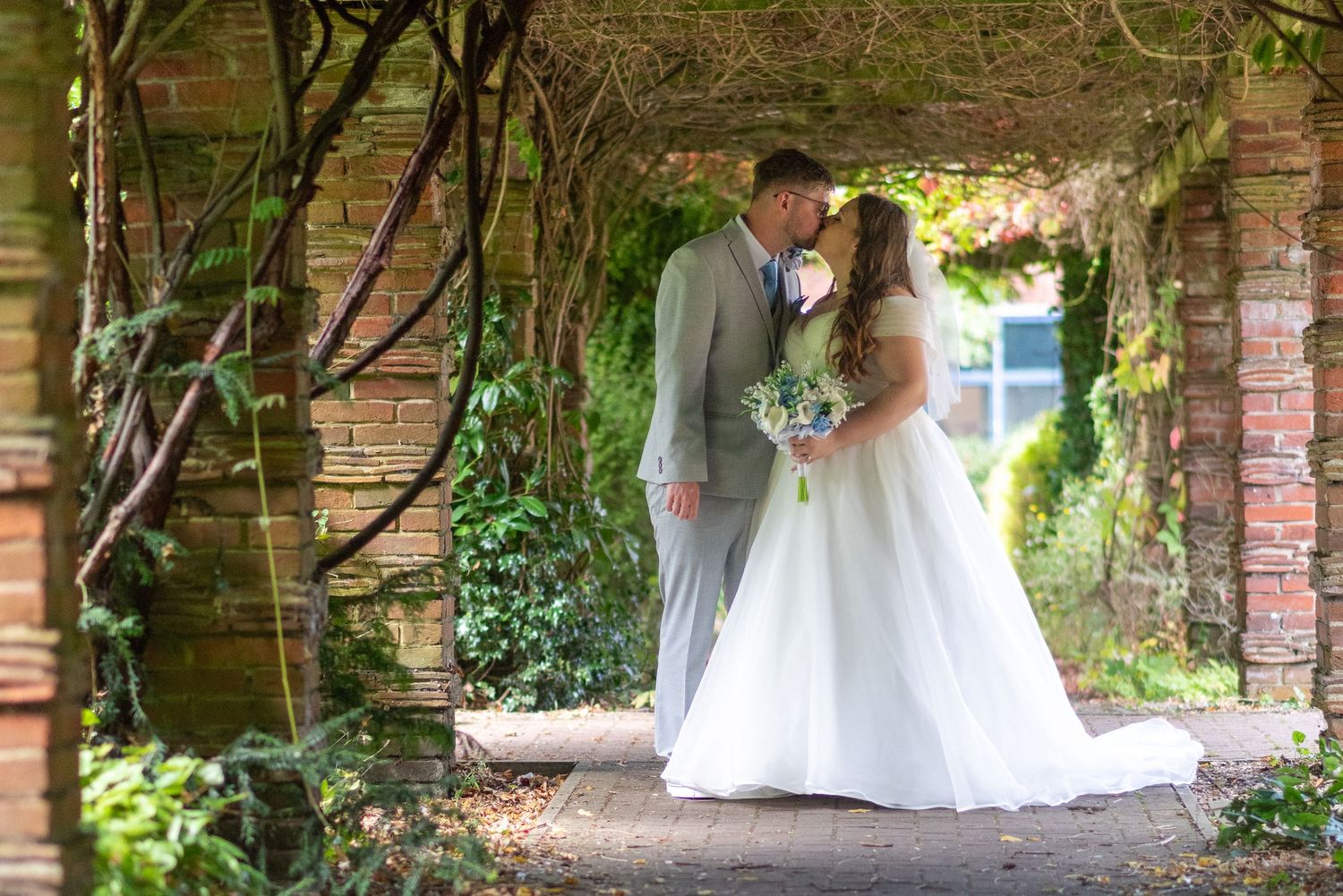 A romantic couple shares a tender moment under a natural ivy-covered archway on their wedding day.