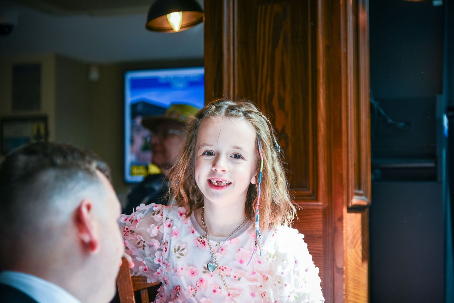 A young girl with wavy hair smiles joyfully at a wedding reception indoor venue.
