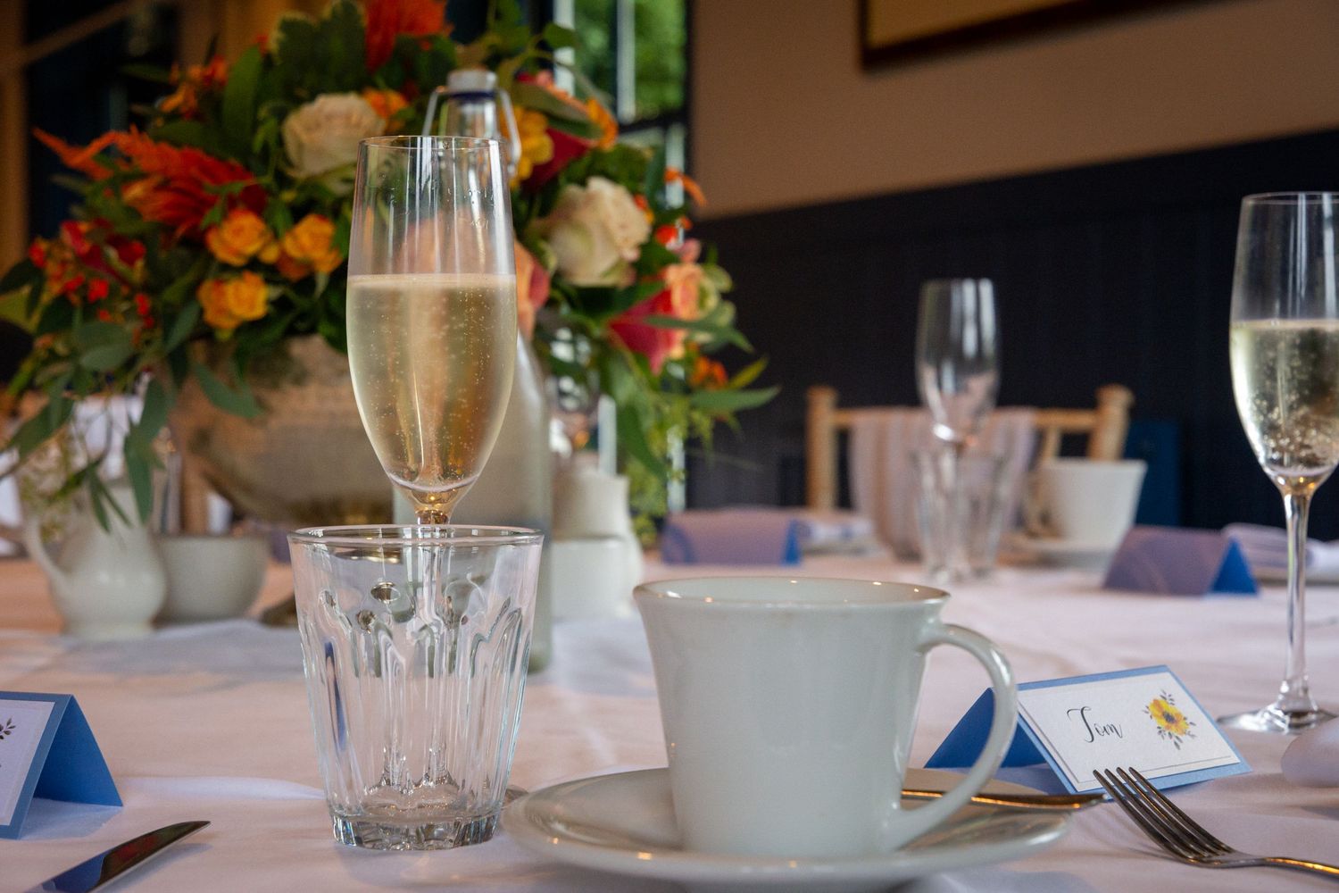 Elegant table setting with champagne flute, teacup, and floral centerpiece at a formal dining event.