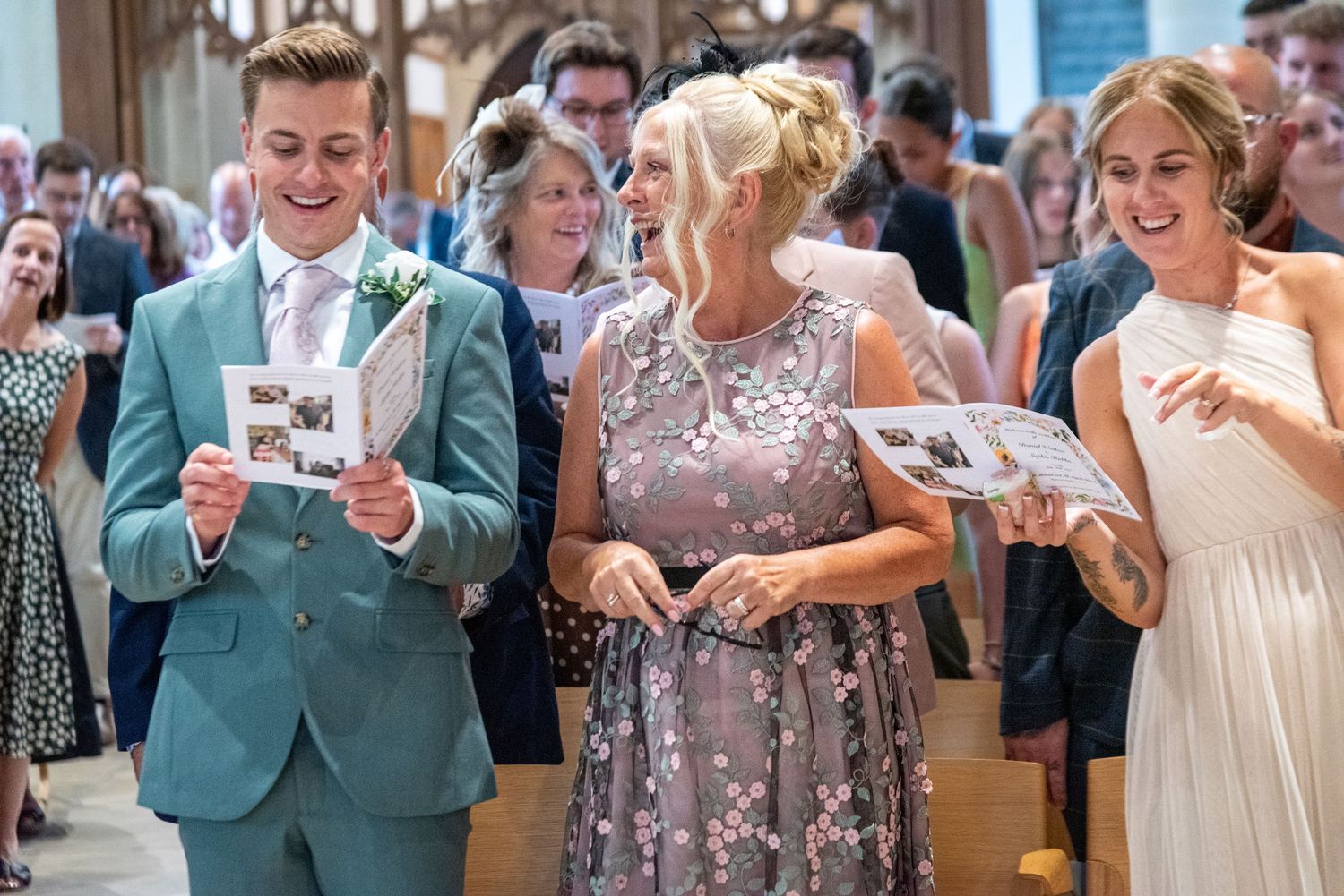 Guests smiling and reading wedding programs while walking down the aisle at an elegant church ceremony.