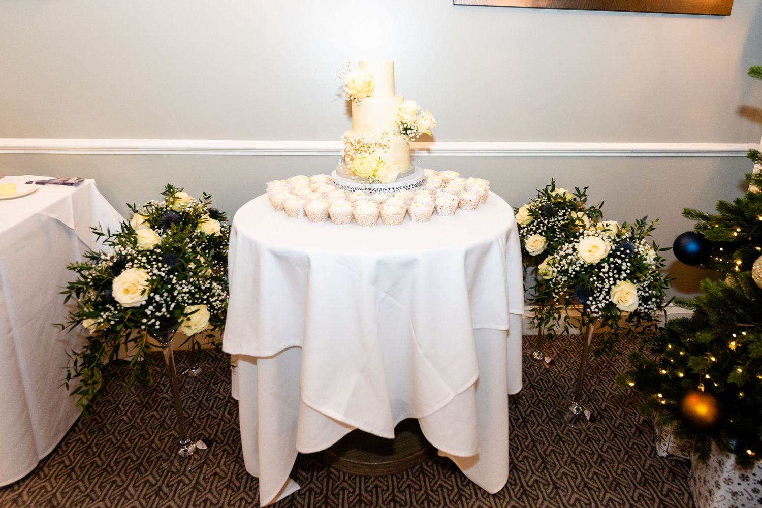 Elegant wedding cake table with white floral arrangements and macarons, decorated for a Christmas reception.