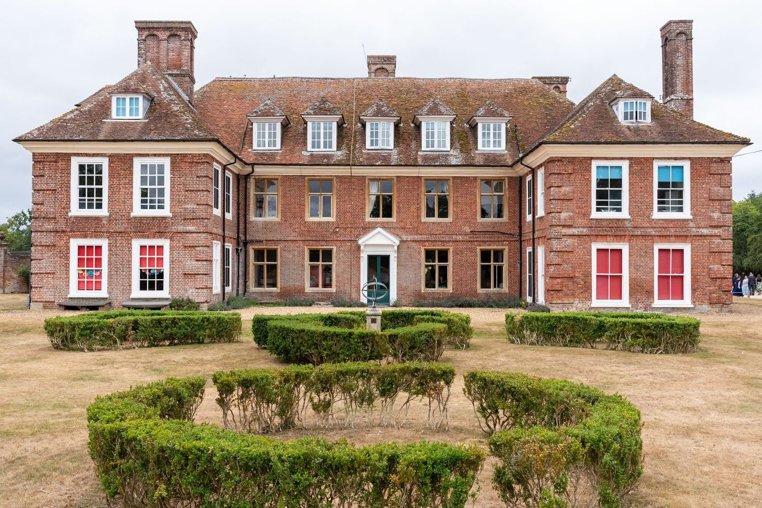 Red brick Georgian manor house with symmetrical facade, white-trimmed windows, and formal hedged garden with ornamental fountain.