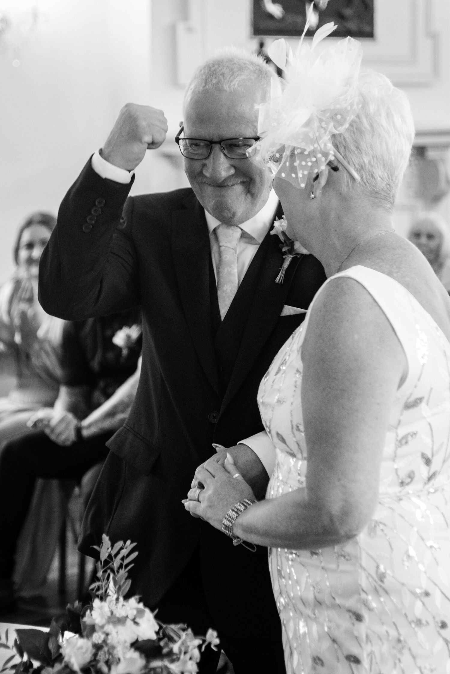 Groom pumps fist in joy beside bride during wedding ceremony, black and white photo.