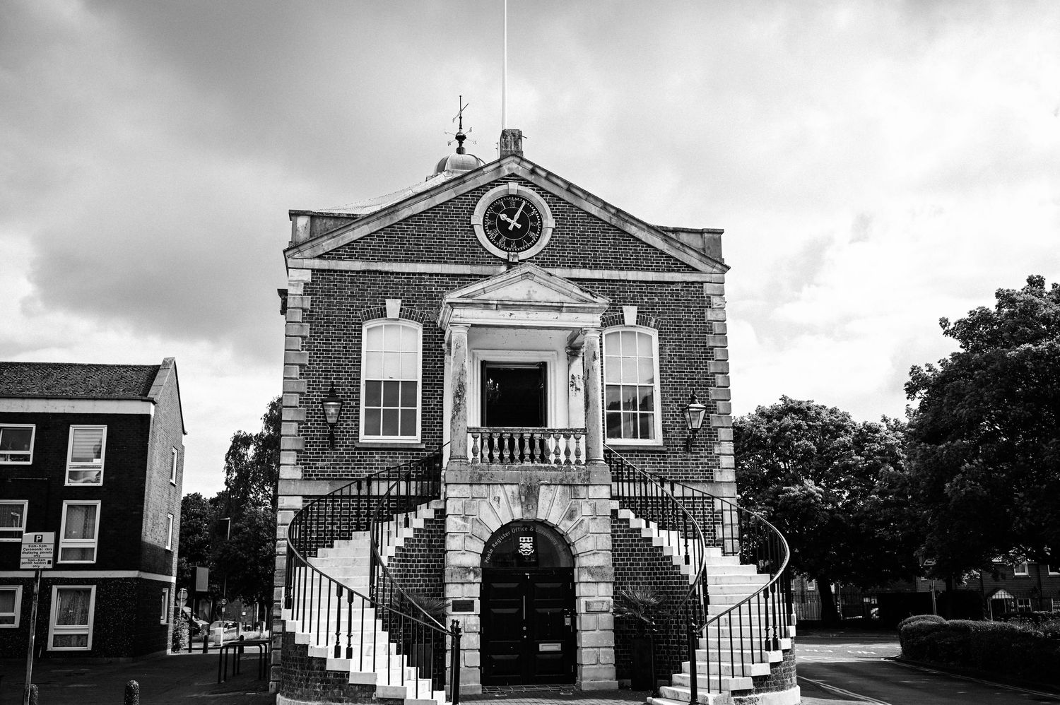 Black and white photo of a historic brick town hall with a clock tower, grand staircase, and columned entrance.