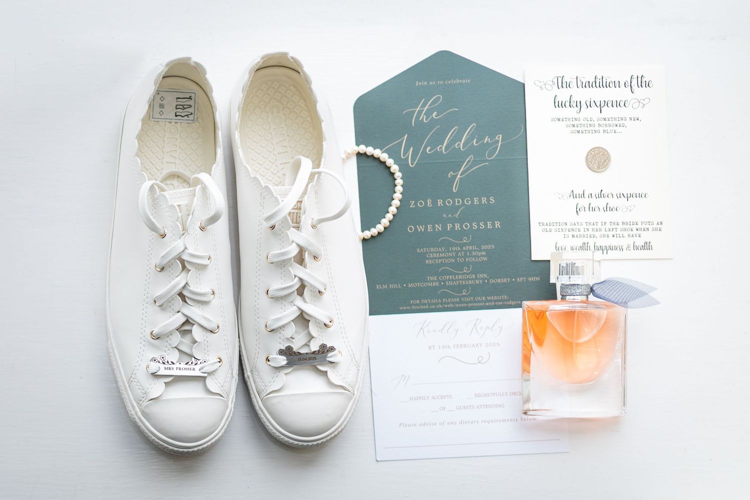 White Converse sneakers, pearl bracelet, teal wedding invitation suite, and orange perfume bottle flatlay.