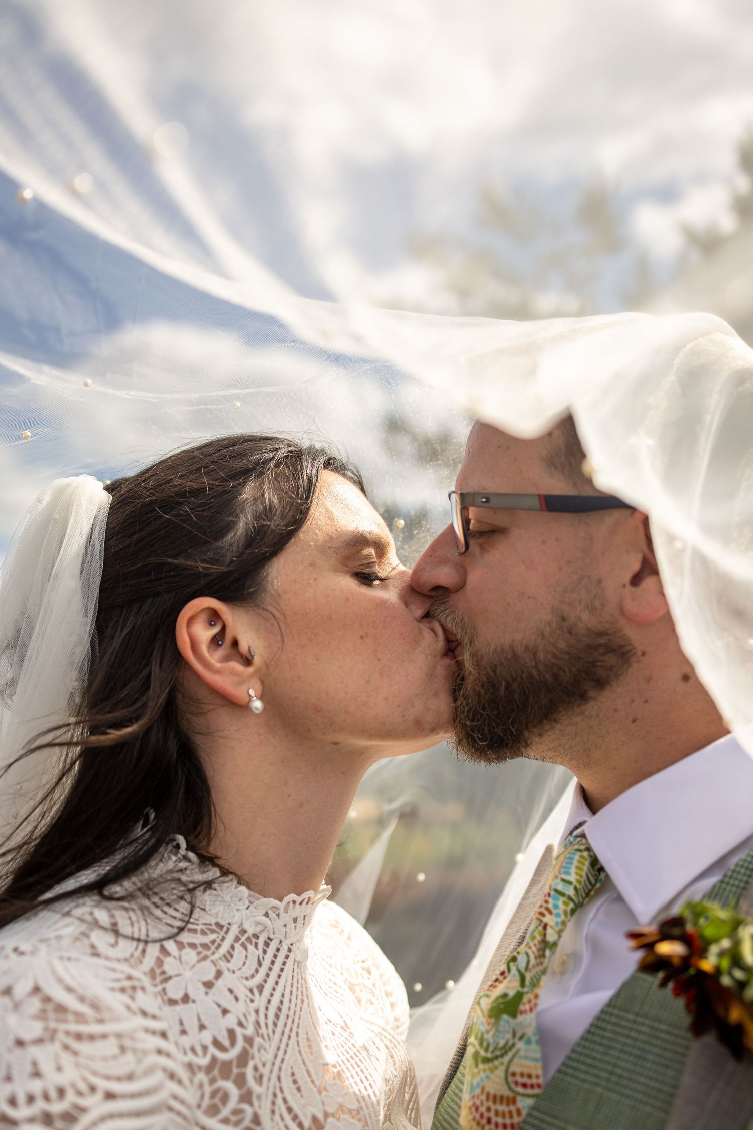 Bride and groom sharing a romantic kiss under a flowing veil on their wedding day.