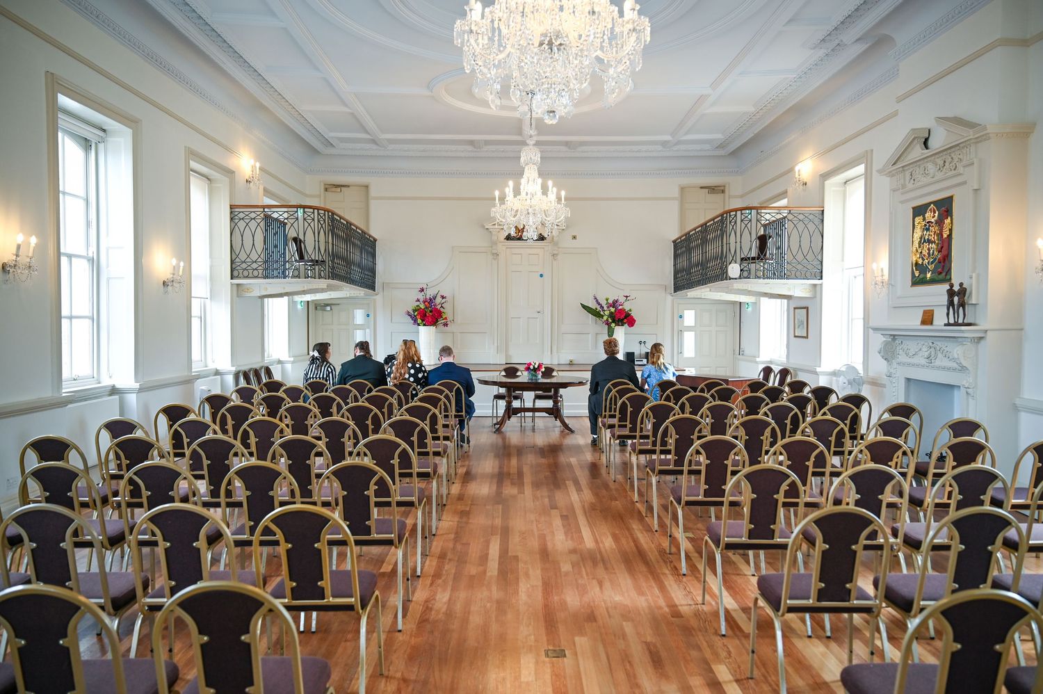 Elegant event hall with chandelier, rows of chairs, hardwood floors, and balcony, set up for a formal ceremony or meeting.
