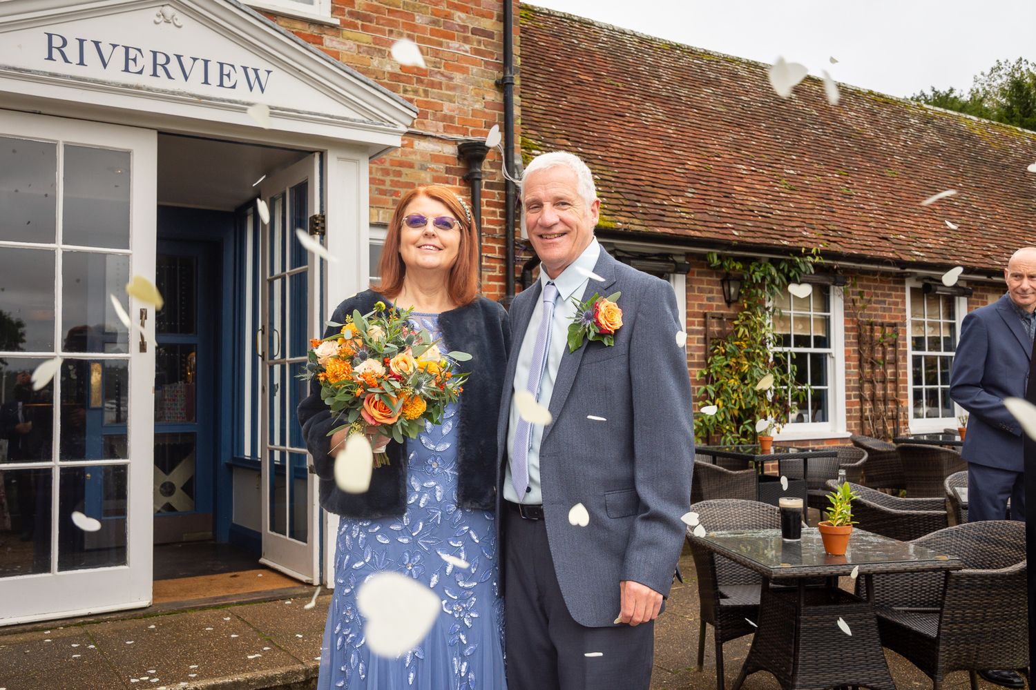 Couple at Riverview venue entrance, woman in blue dress with autumn bouquet, man in grey suit.