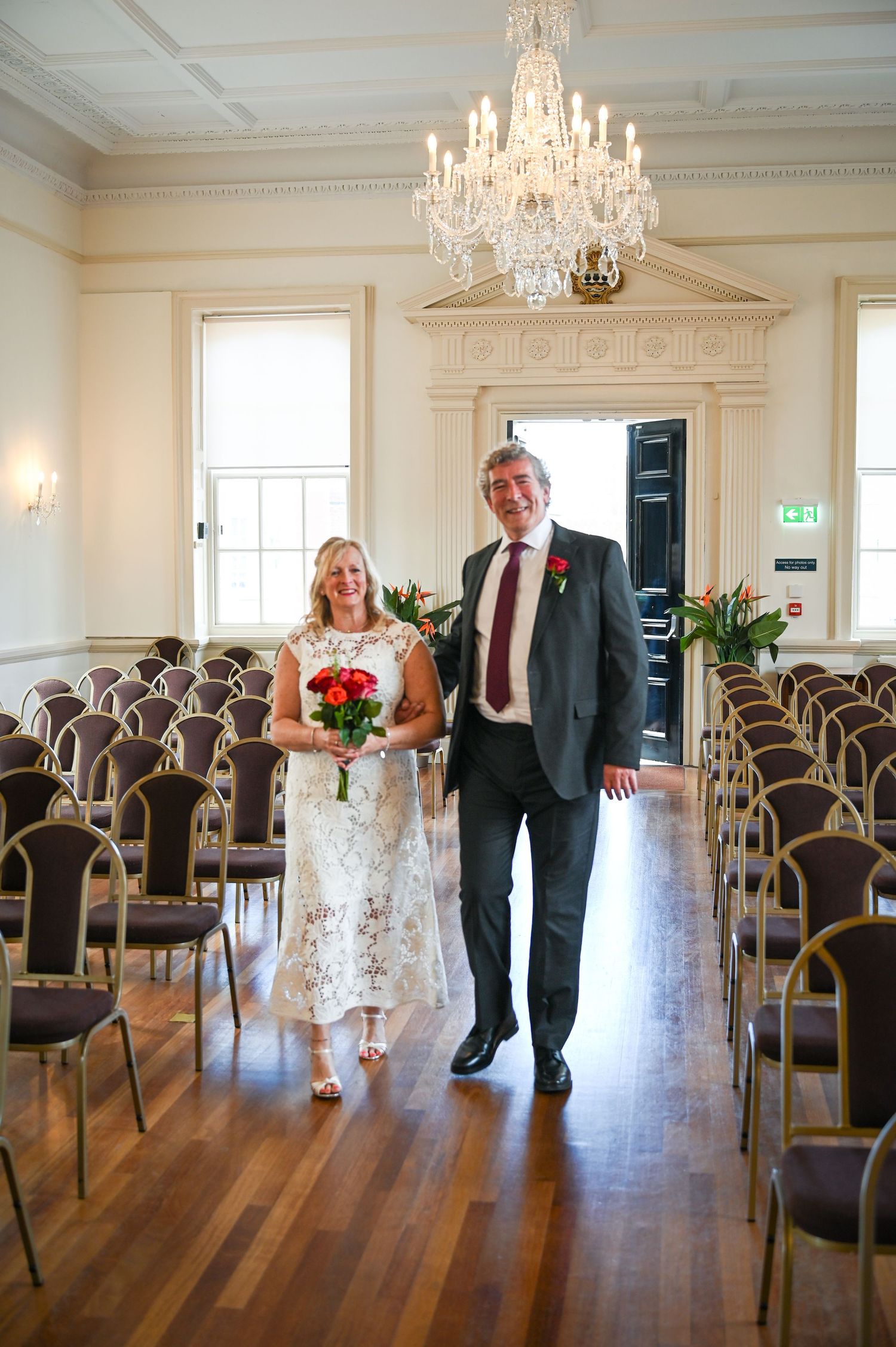 Bride and groom walking down the aisle in an elegant wedding venue with chandelier and wooden floors.