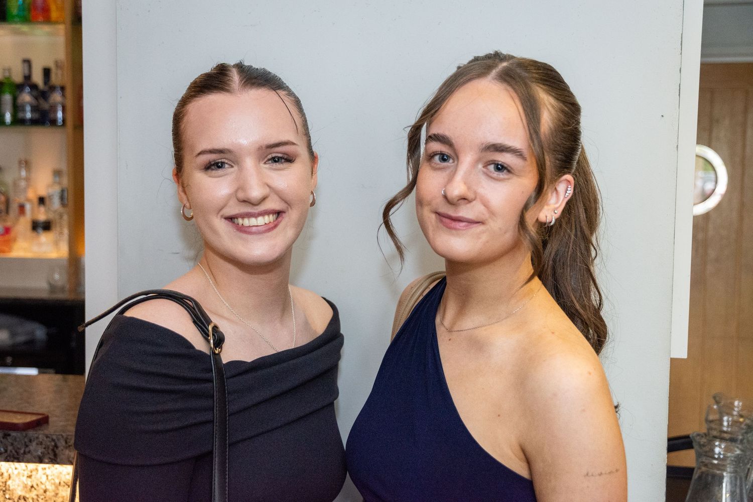 Two young women in elegant dresses smiling at a formal event.