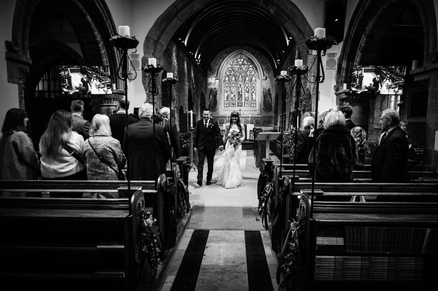 Black and white wedding ceremony photo inside a historic church with couple at the altar and guests seated in pews.