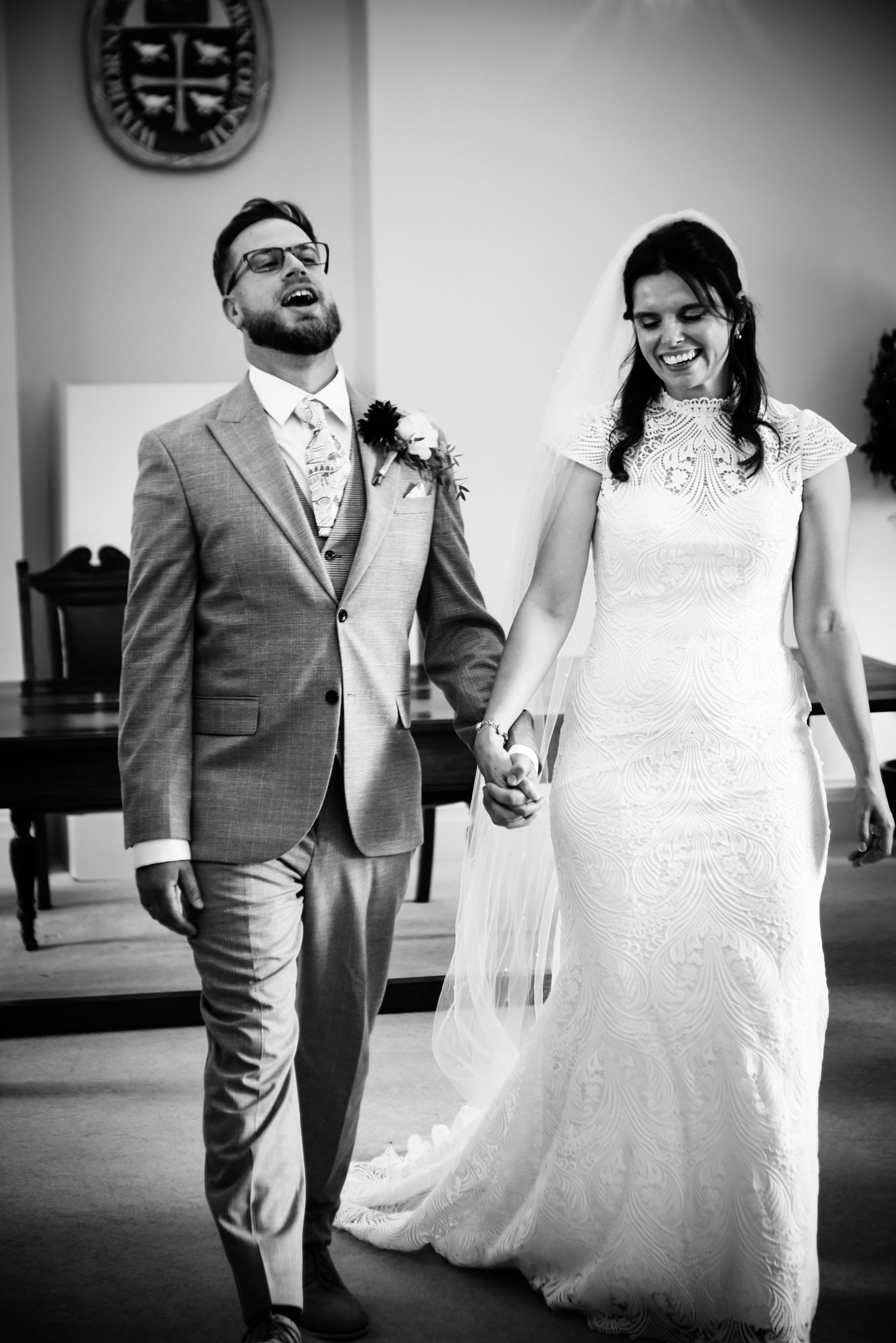 Black and white photo of a smiling bride and groom holding hands walking down the aisle after their wedding ceremony.
