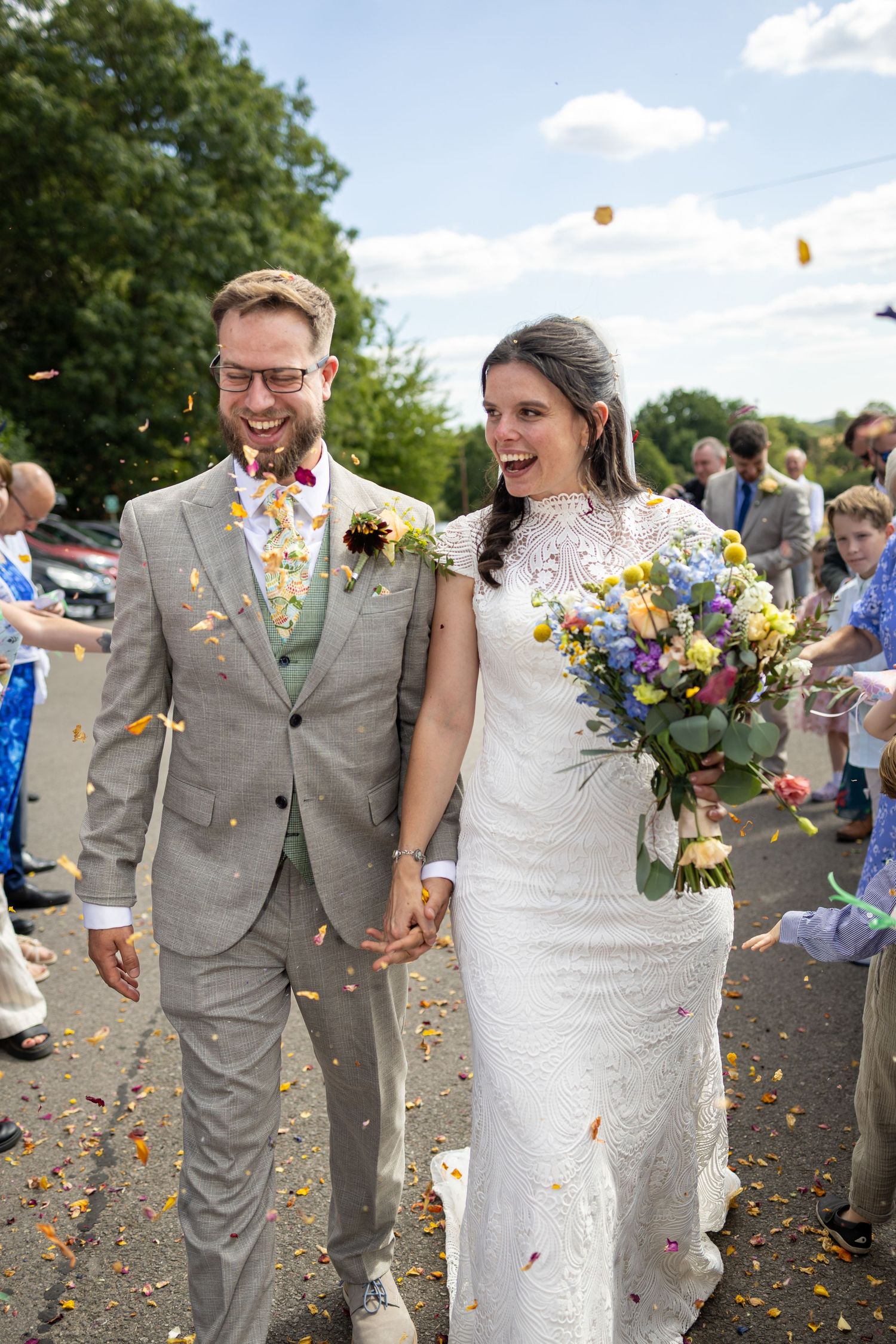 Joyful bride and groom walk hand in hand through a shower of colorful confetti thrown by wedding guests outdoors.
