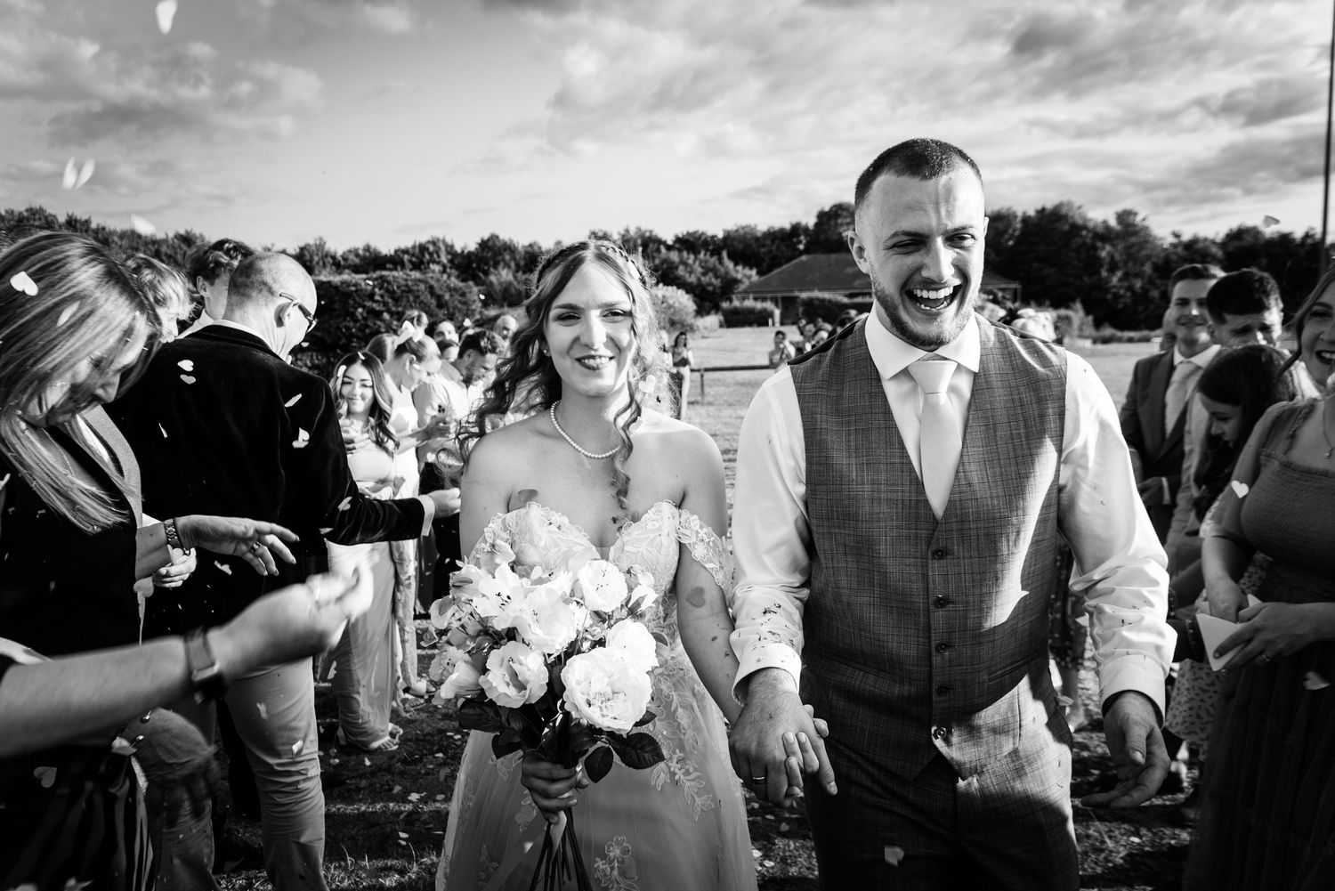 Wedding guests celebrate and dance together at an outdoor reception under a cloudy sky.
