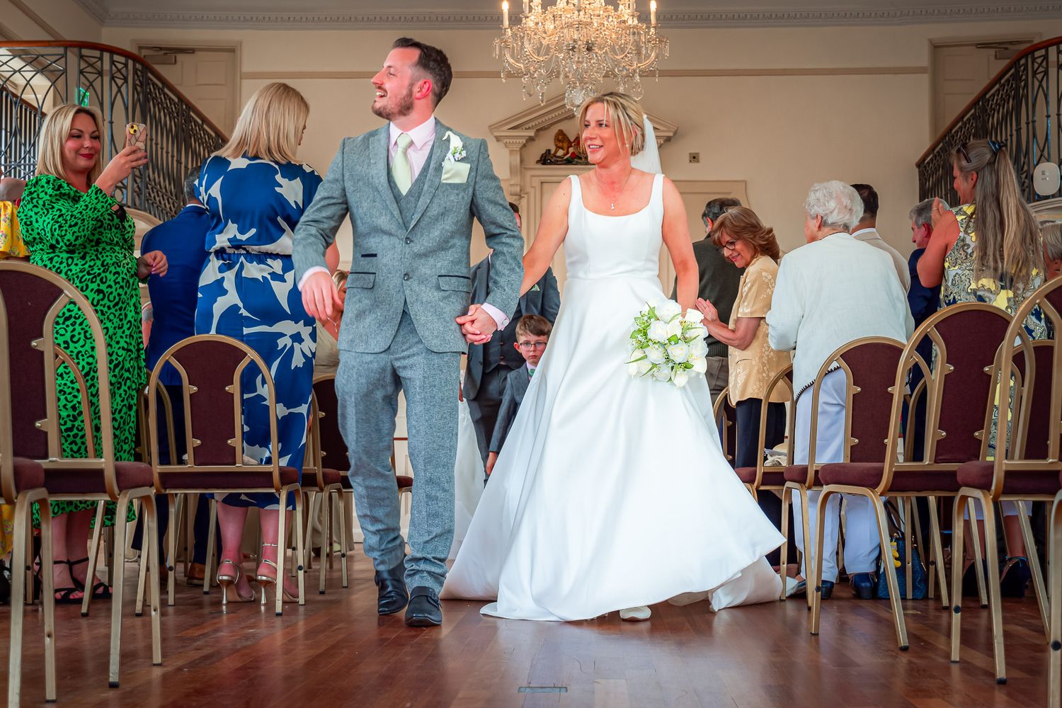 Dancing couple celebrates during wedding reception in elegant venue with chandelier and vintage chairs.