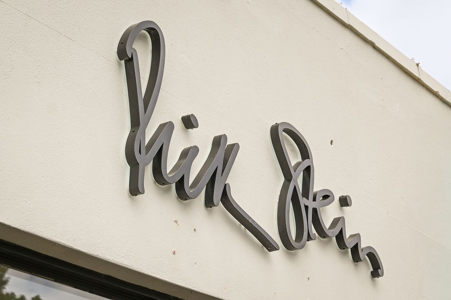 Close-up of Hin Hin restaurant cursive metal sign mounted on a white exterior wall.