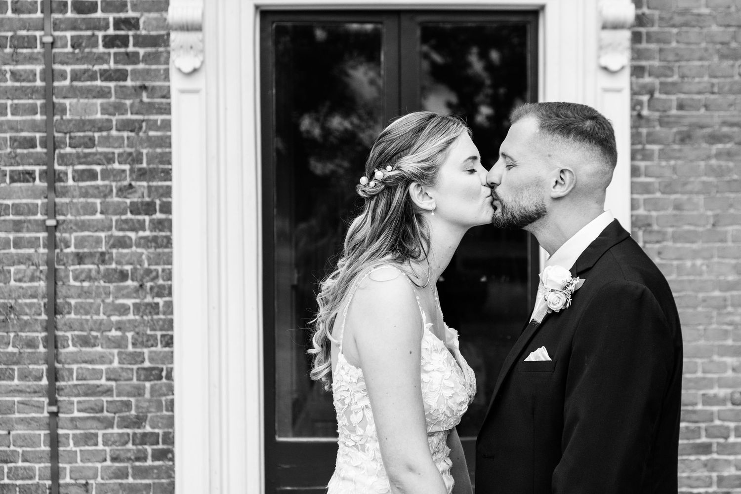 Black and white photo of a bride and groom sharing a kiss outside a brick building on their wedding day.