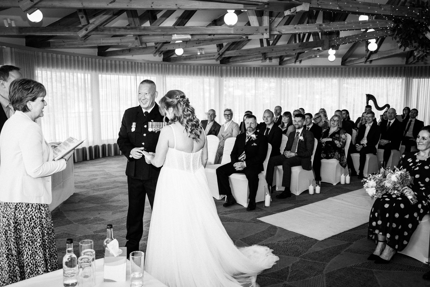 A bride and groom exchange vows during an indoor wedding ceremony with seated guests in a elegant venue.