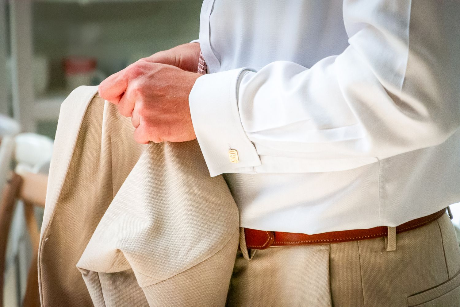Man in white dress shirt and tan suit holding jacket with brown belt visible at waist.