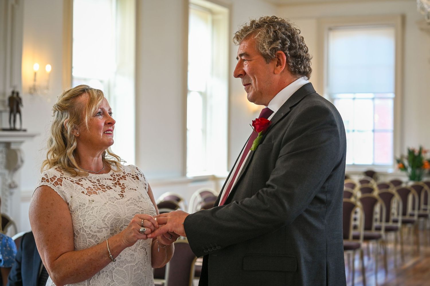 Bride and groom exchange rings during wedding ceremony in elegant venue, smiling joyfully.