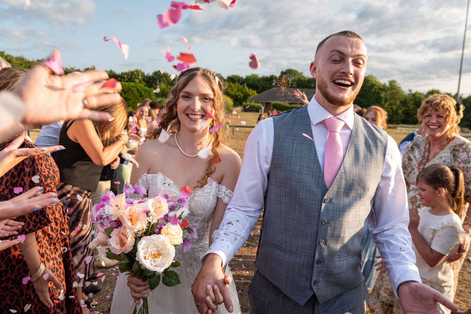 Happy couple walking through confetti shower outdoors after their wedding ceremony.