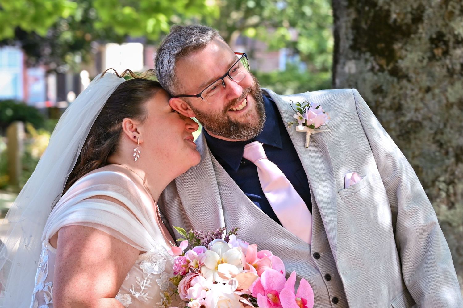 Happy bride and groom sharing a romantic moment outdoors, bride holding pink bouquet, groom in gray suit with pink tie.