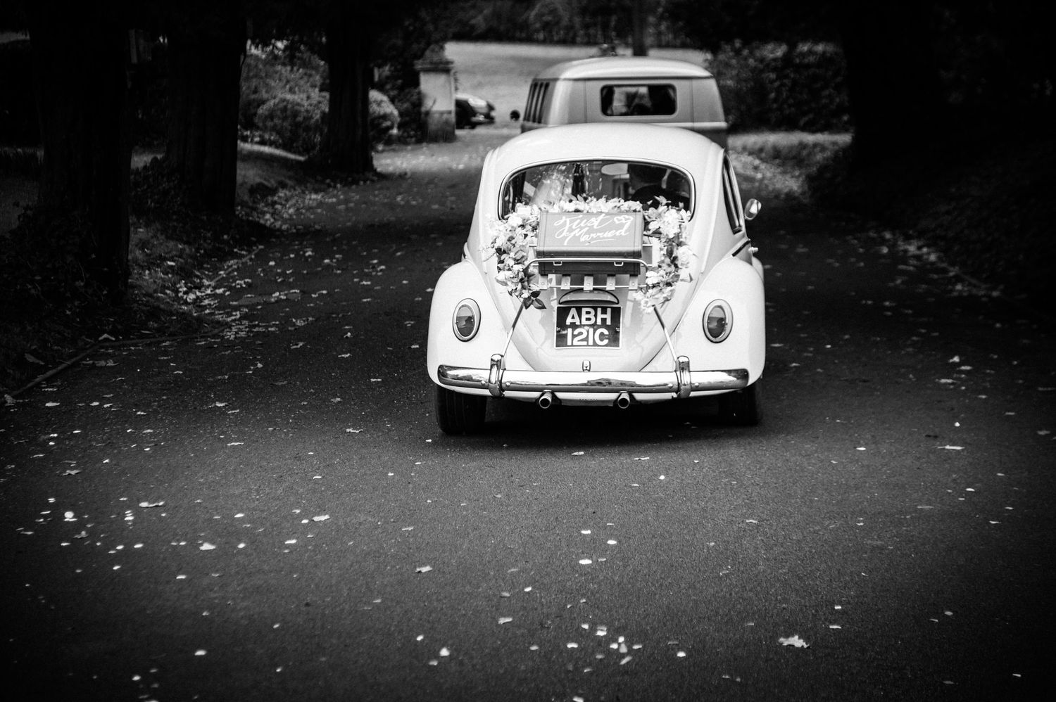 A line of classic vintage cars parked in black and white photography with fallen leaves scattered on the ground.