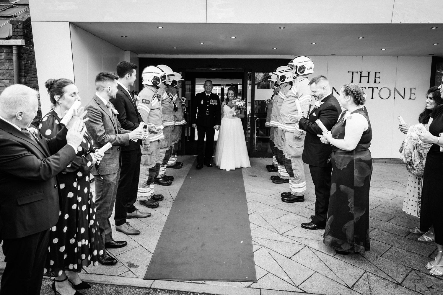 Bride and groom exit The Keystone venue through a guard of honour in black and white wedding photo.