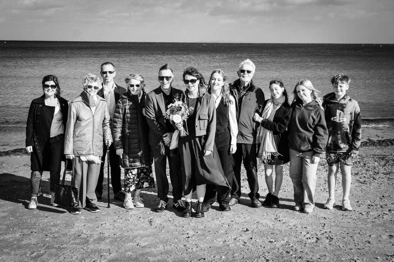 A black and white panoramic sequence showing a line of people walking along a beach shoreline.